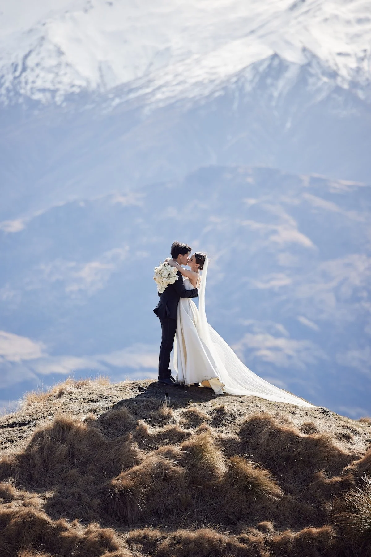 Bride and groom embracing on a mountaintop during a New Zealand destination wedding, captured by Lost in Love Photography.