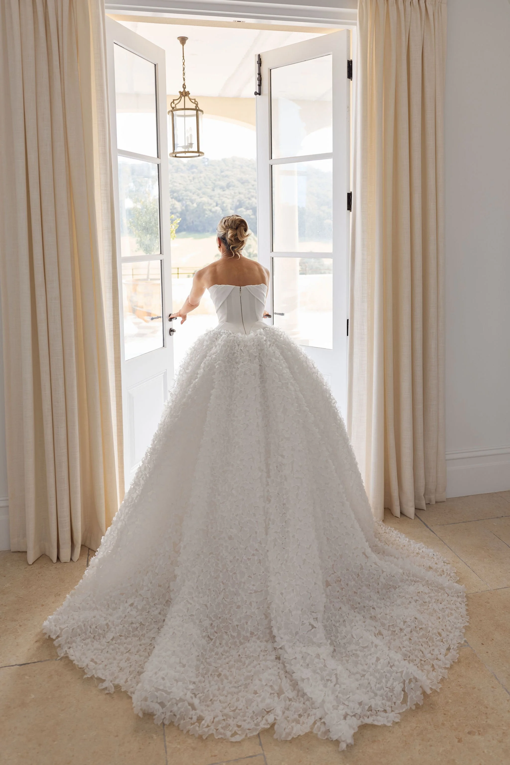 Bride in sculptural white wedding gown photographed through French doors