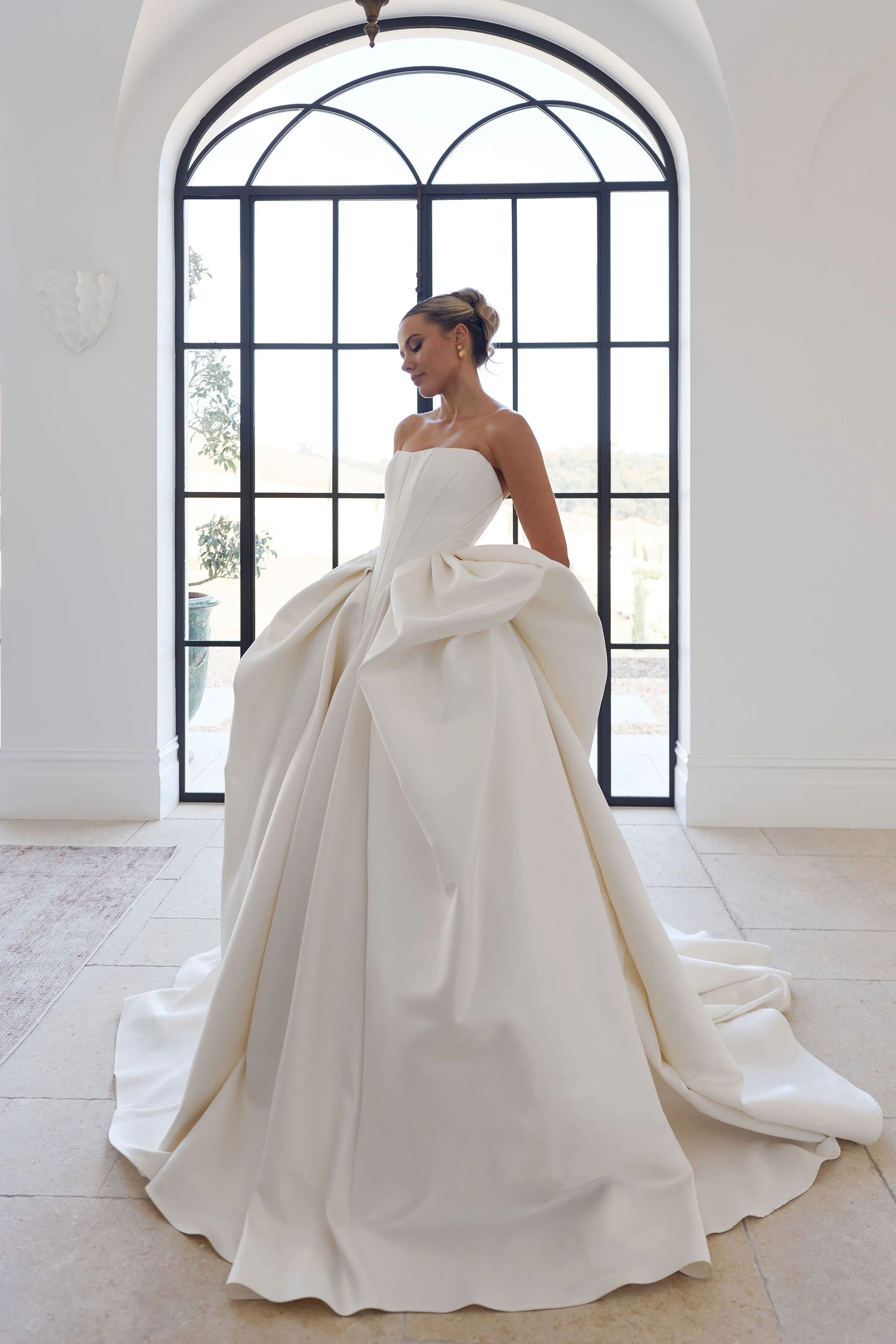 Bride in voluminous white gown beneath arched architectural window