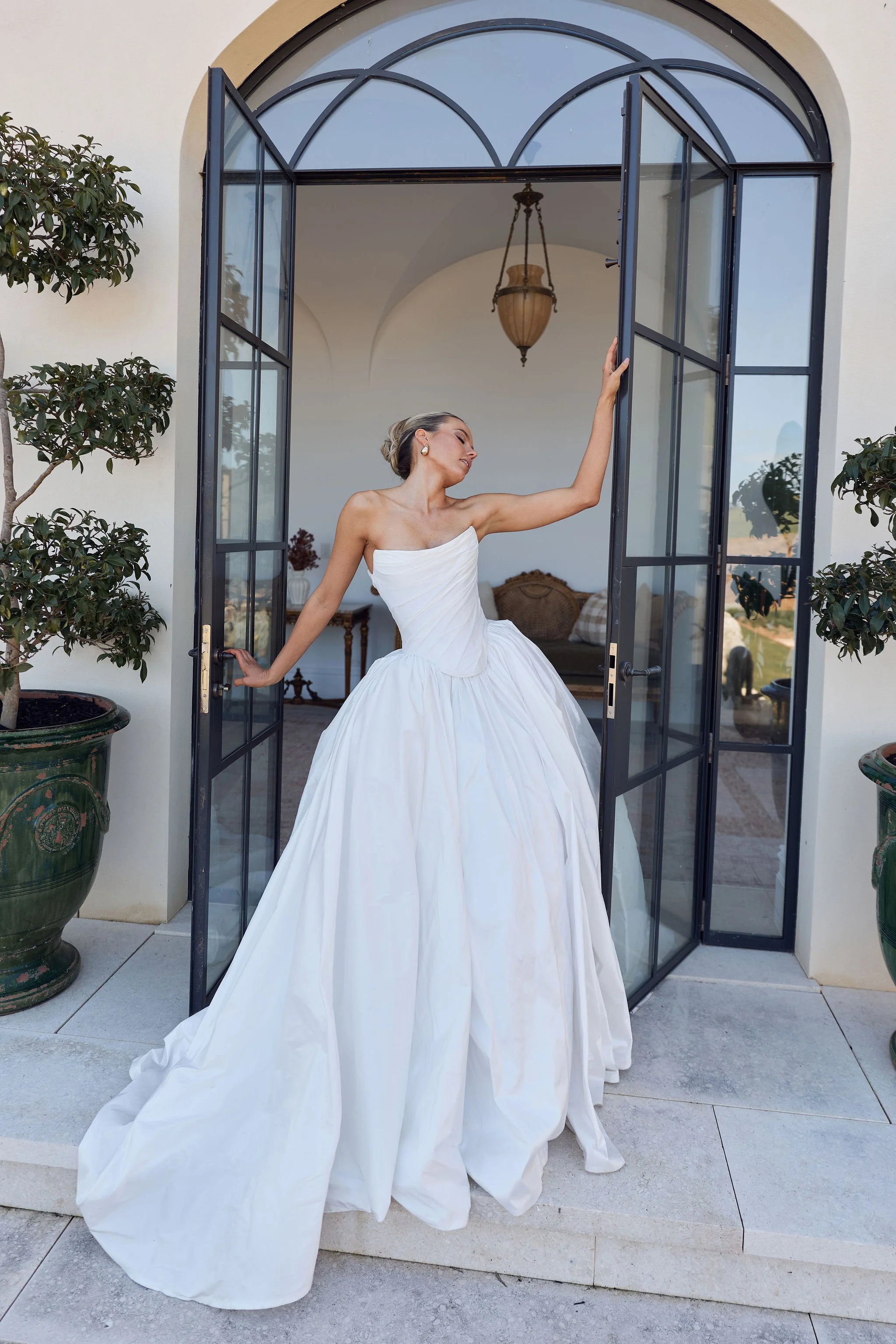 Bride in voluminous white gown beneath arched architectural window