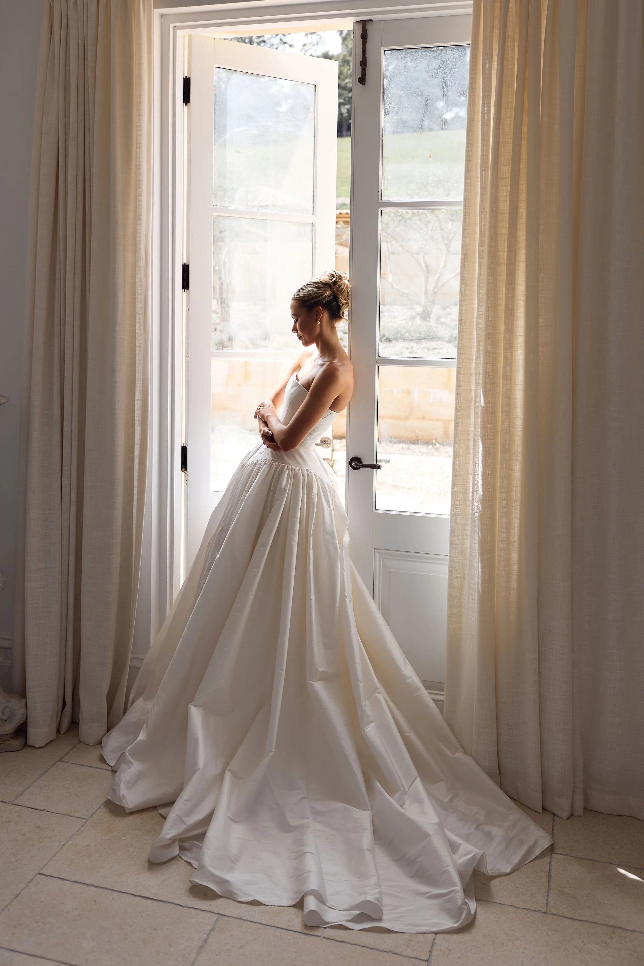 Bride in sculptural white wedding gown photographed through French doors