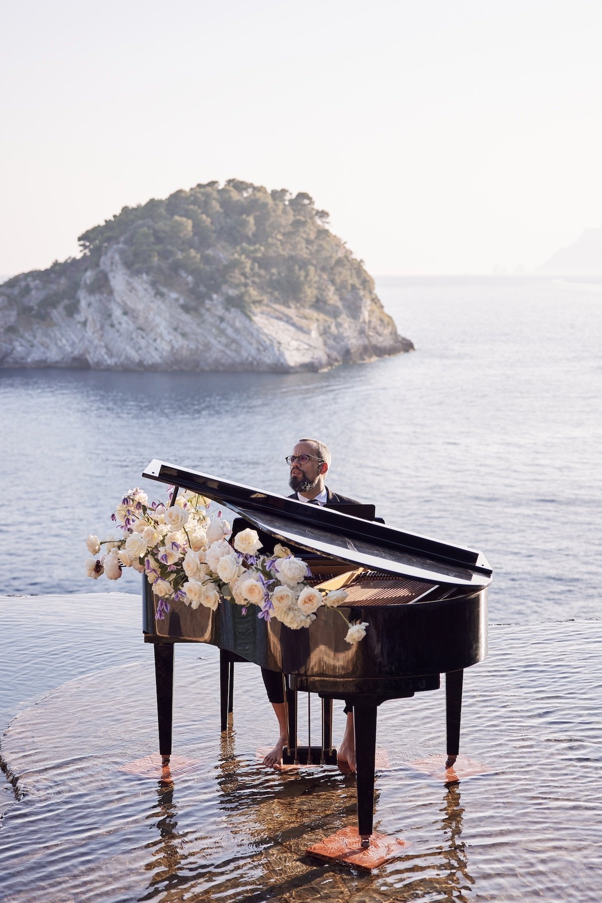 Grand piano set at the water’s edge beside a luxury island wedding reception with dramatic coastal views.