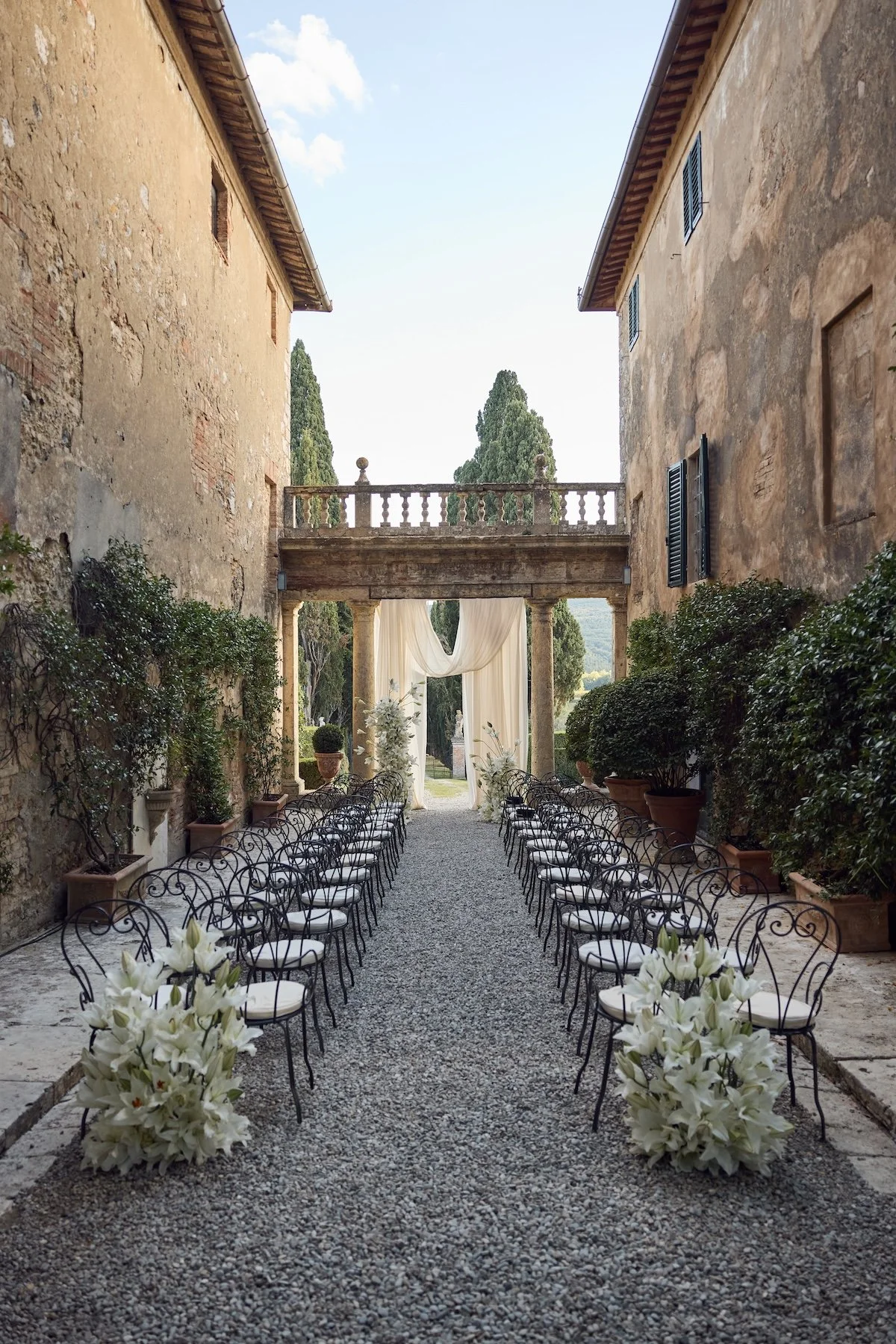 Stone courtyard wedding ceremony aisle at a Tuscan wedding venue with floral arrangements and historic architecture.