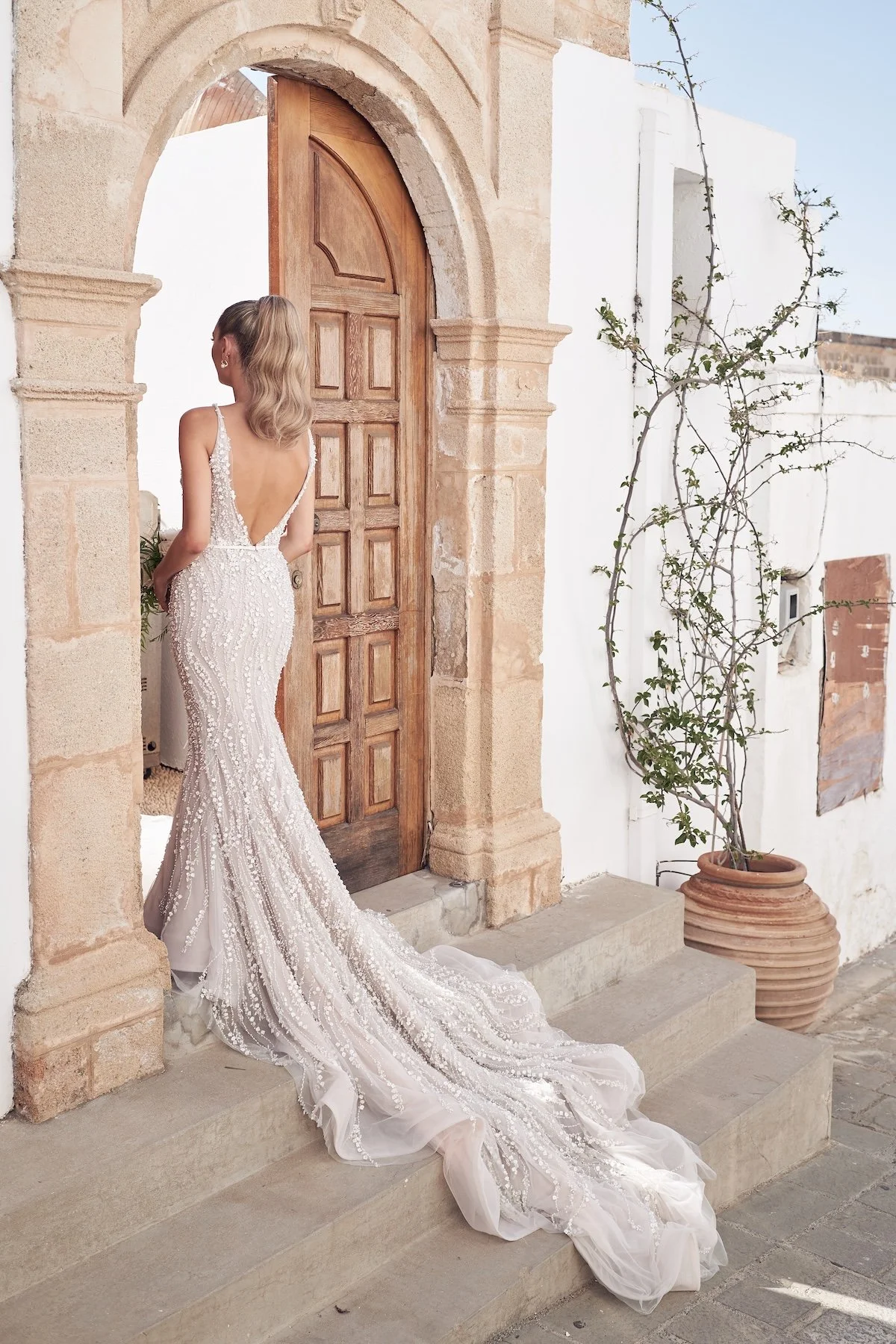 Bride posing in a sleek wedding gown at an arched stone doorway with Mediterranean-inspired architecture.
