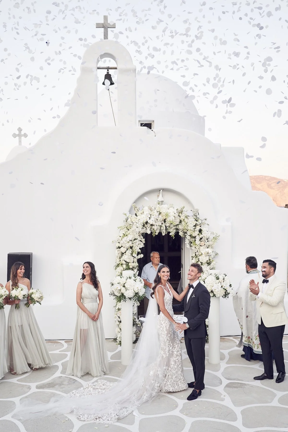 Wedding ceremony outside a whitewashed church with floral decor in Santorini, Greece, captured by Lost in Love Photography.
