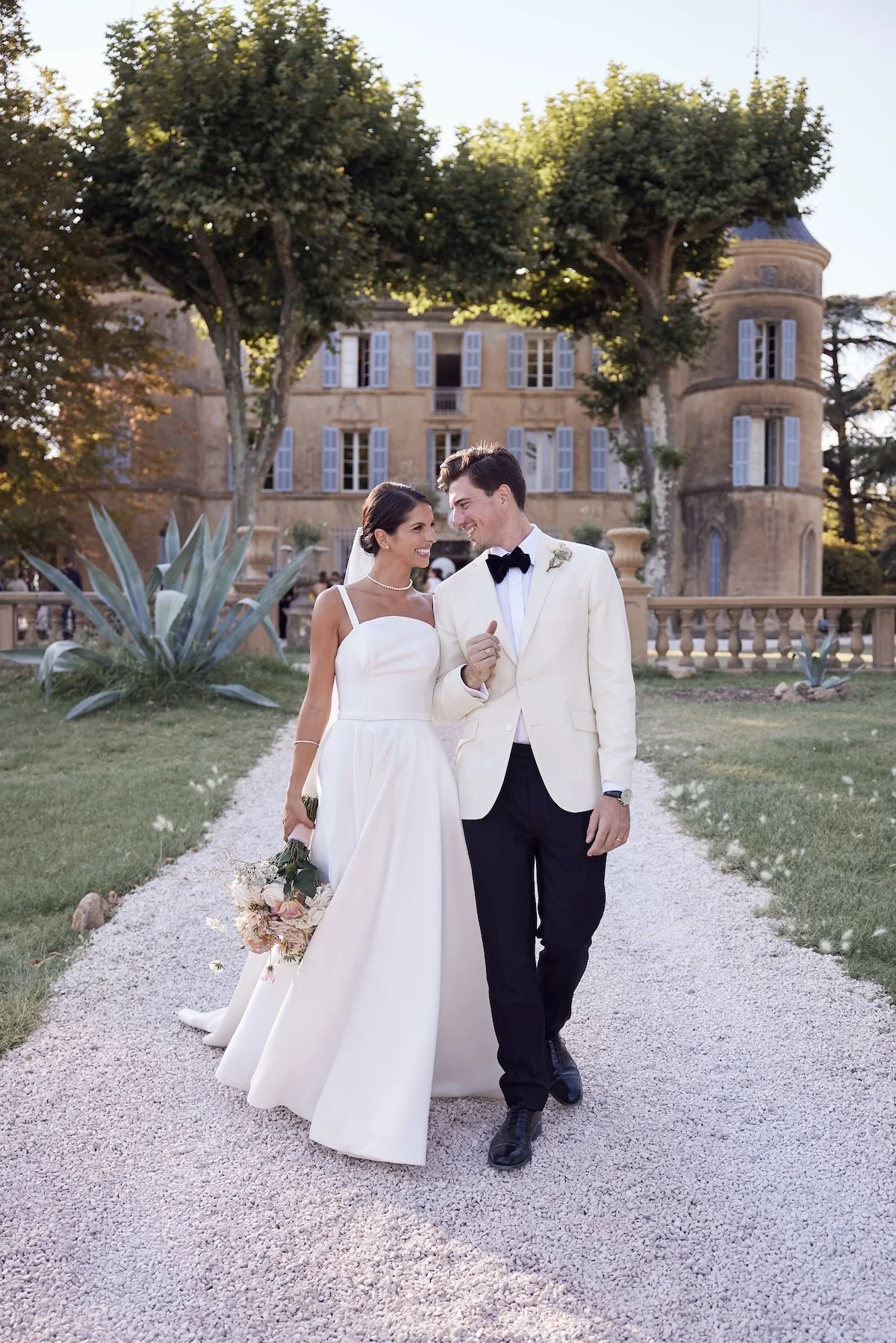 Bride and groom walking together through the gardens of a French Riviera wedding venue at golden hour.