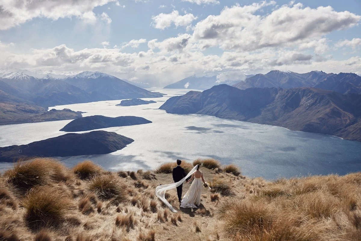 Wedding couple walking at Coromandel Peak, at Lake Wanaka with panoramic mountain views in New Zealand.