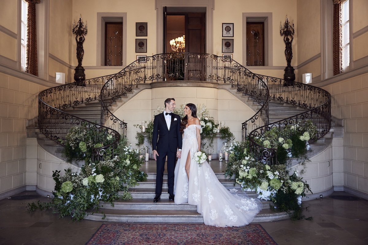 Bride and groom standing on a grand staircase inside a historic New York estate wedding venue.
