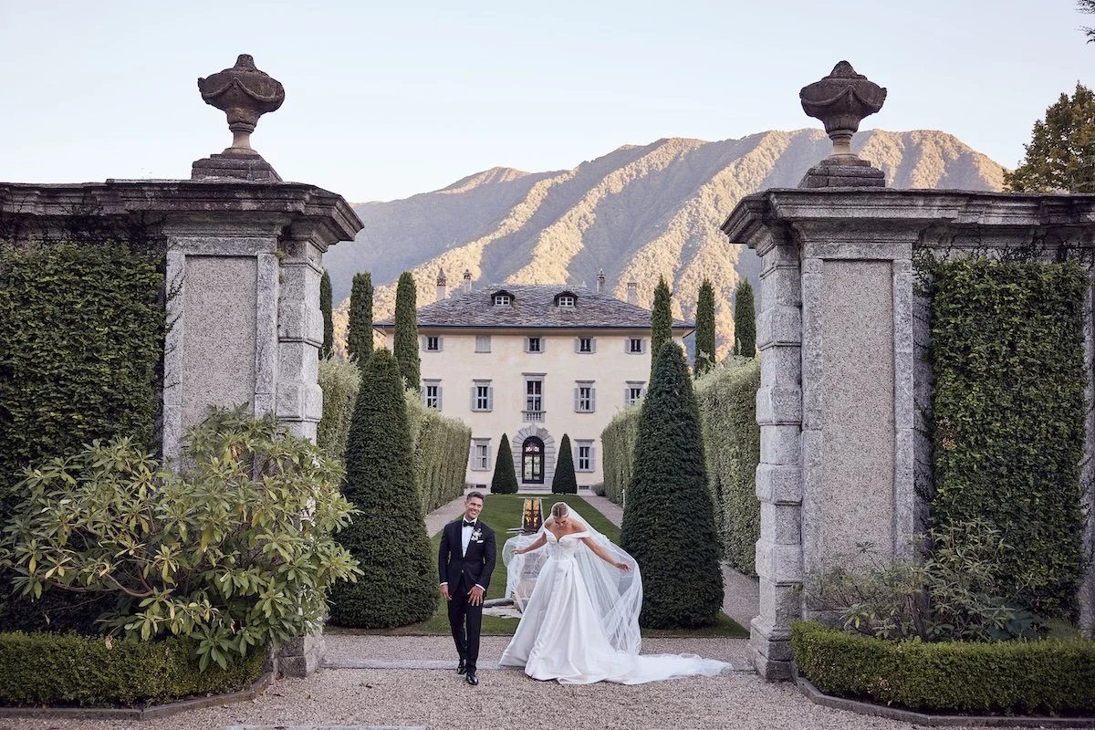 Bride and groom walking through the gates of a historic Italian villa surrounded by estate gardens.