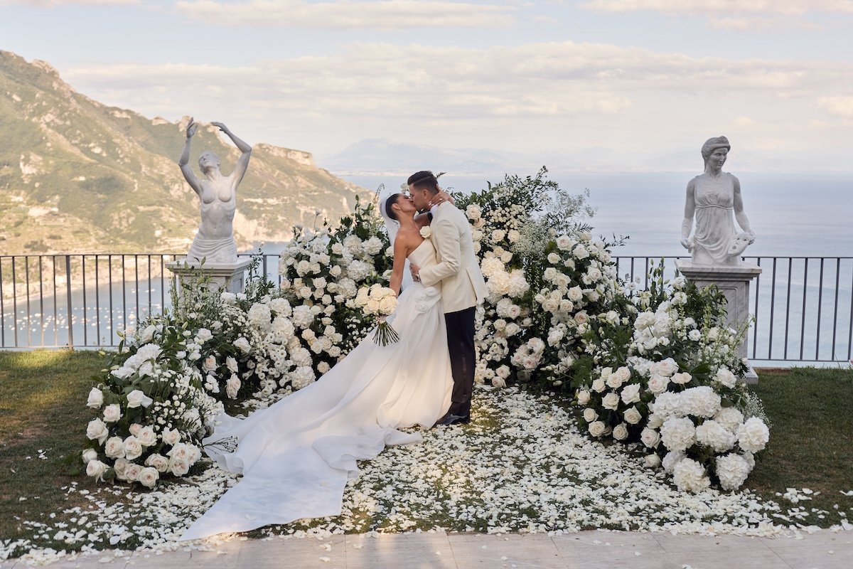 Bride and groom kiss at an outdoor Lake Como wedding ceremony with white florals and lake views captured by Lost in Love Photography.