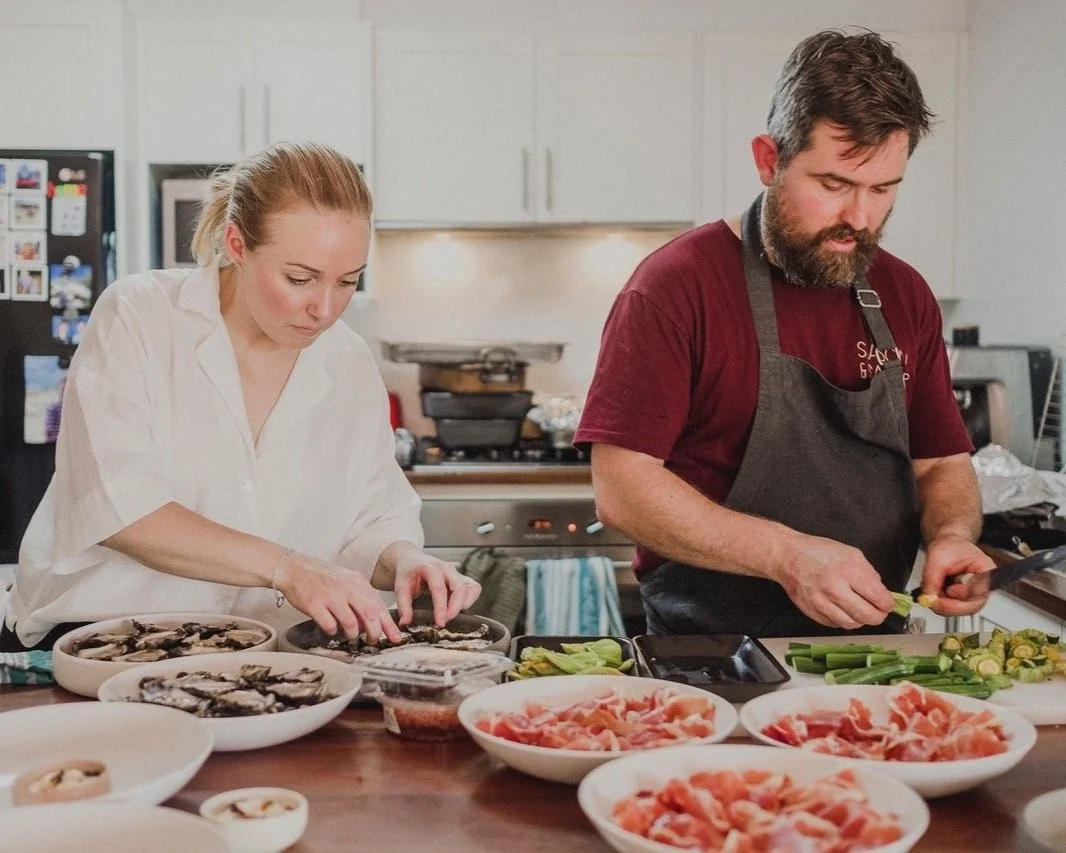 Liz and Sean preparing food in a private kitchen, with various bowls of chopped ingredients on the counter.