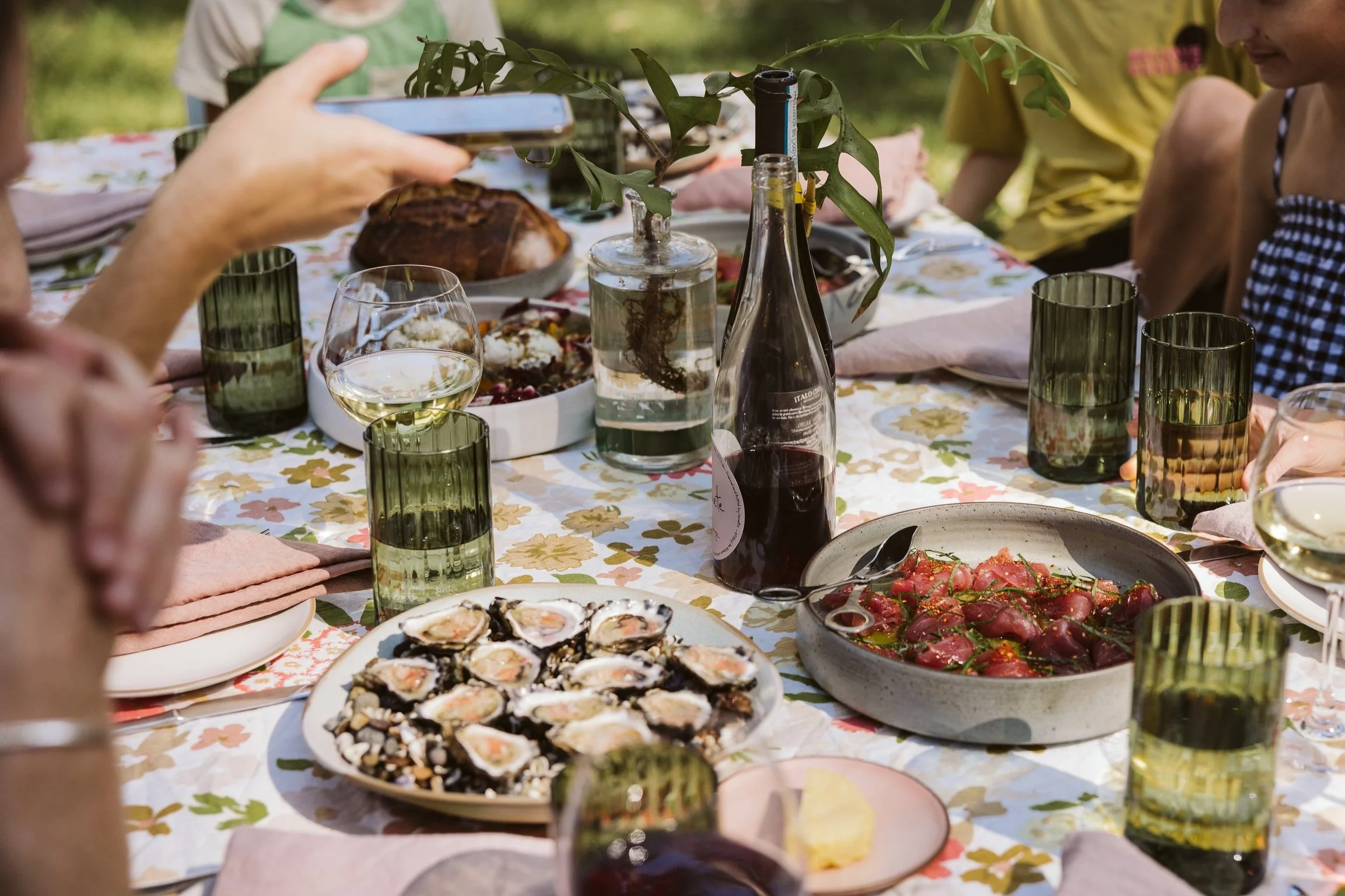 alt="A family and friends enjoying a delicious private dining experience, sitting around a table laid with fresh linen, sharing plates of oysters, burrata and fish crudo, enjoying wine and sharing food. "