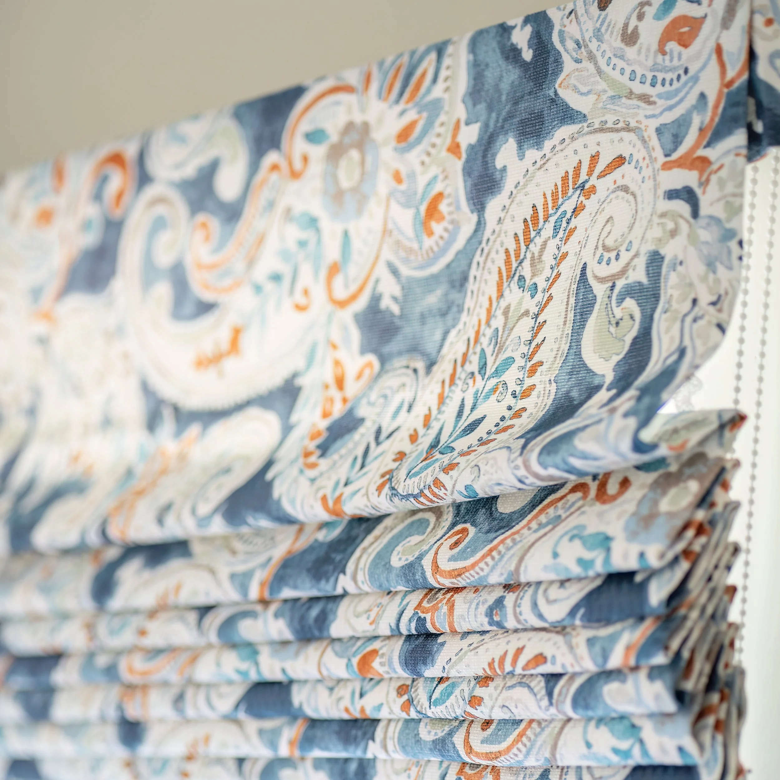 Stacked fabric blinds with a blue, white, orange, and beige paisley pattern.