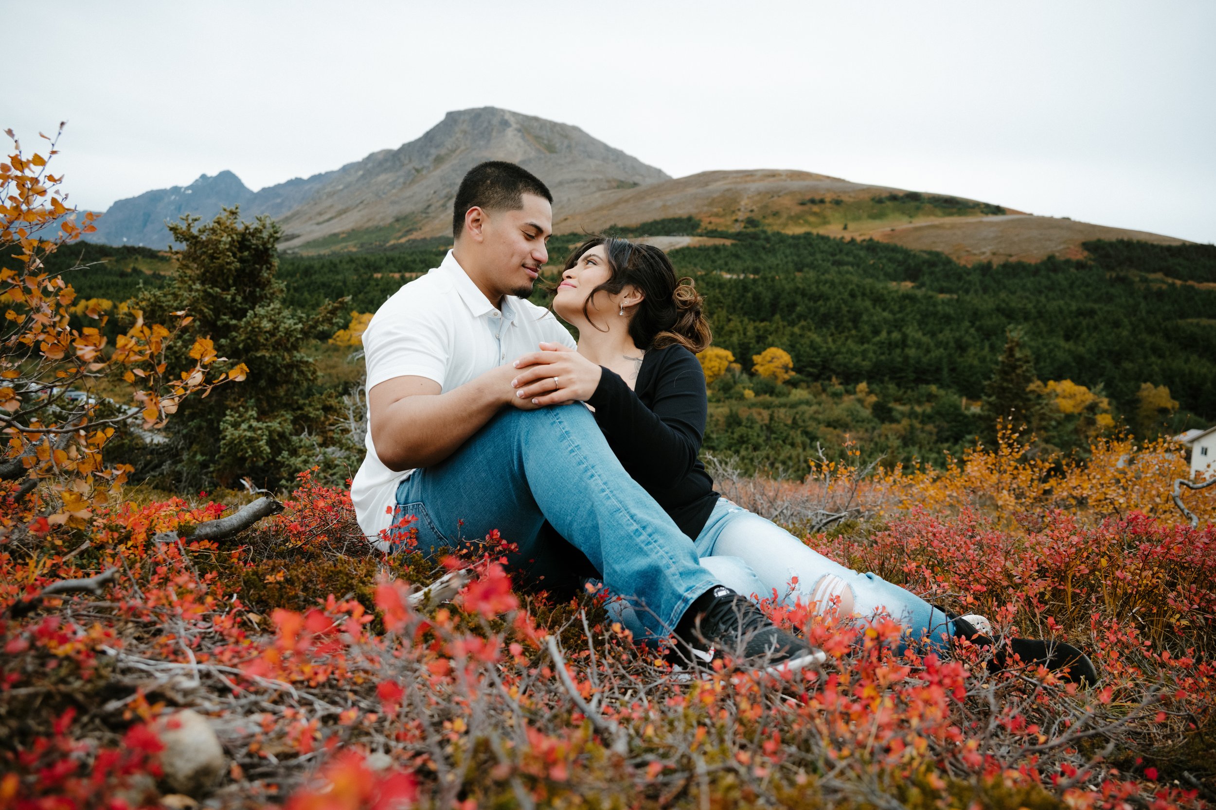Couple sitting in an autumn landscape with colorful foliage and mountains in the background.