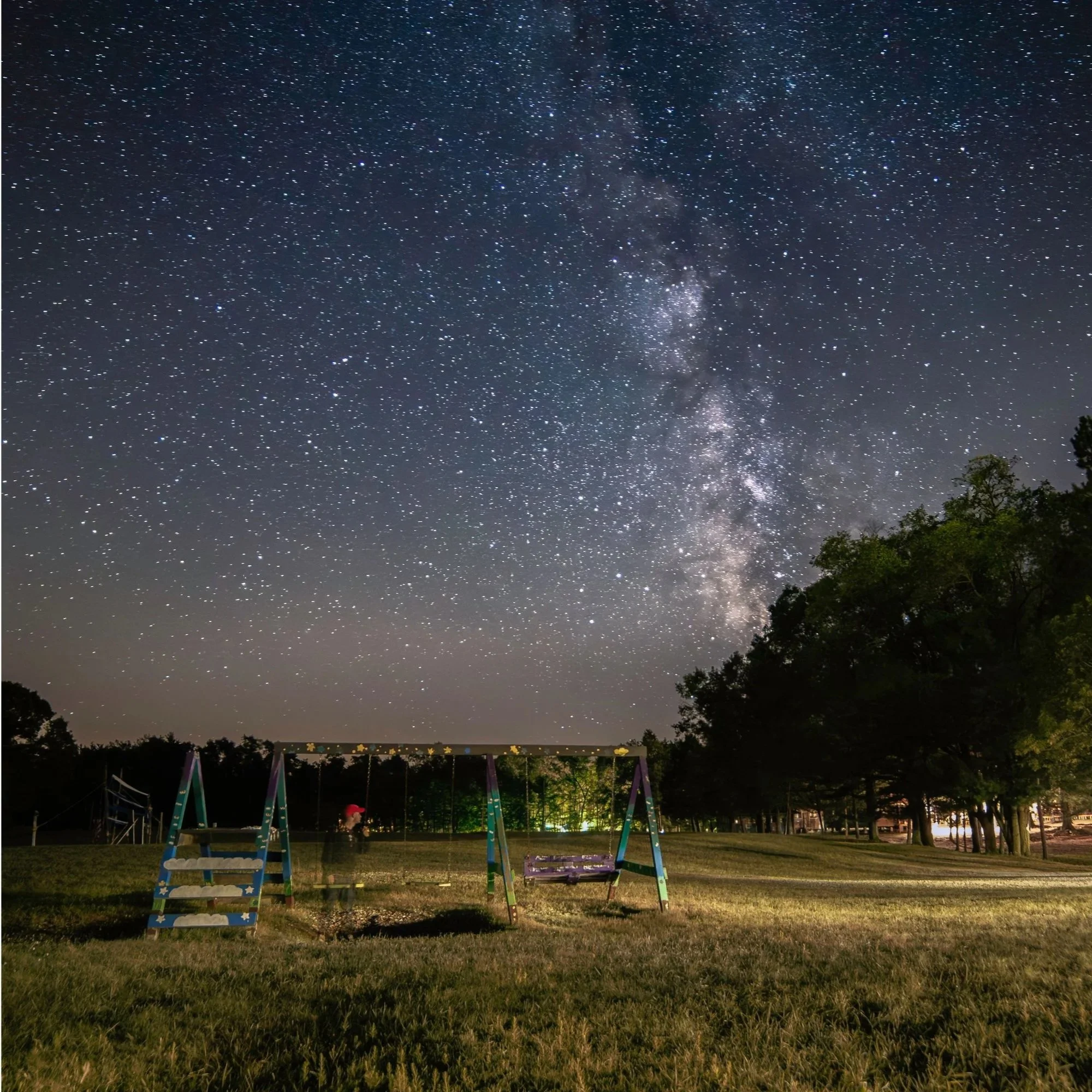 Night sky filled with stars and the Milky Way galaxy, with a playground featuring swings in the foreground.