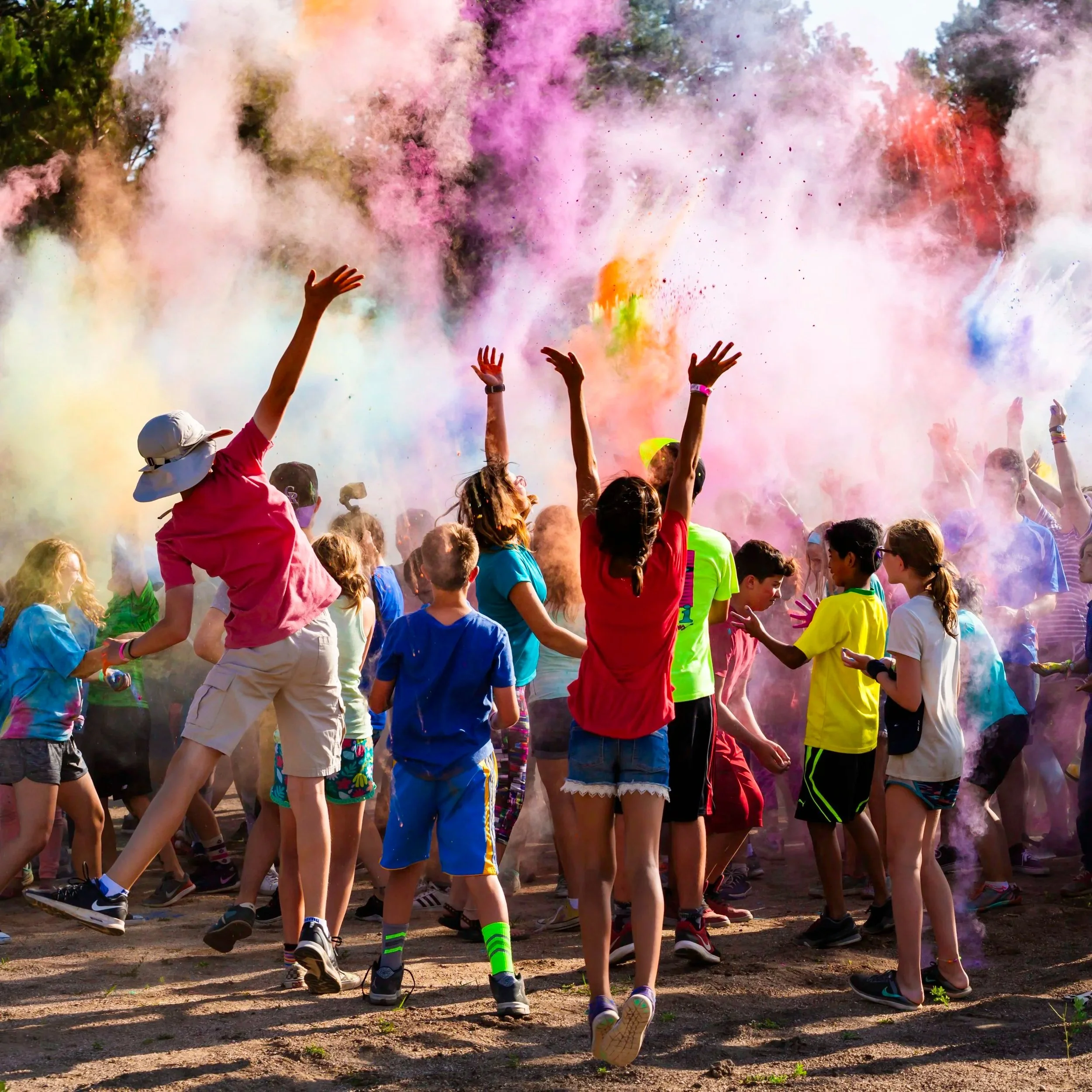 Crowd of people participating in a color run, with multicolored powder in the air and on their clothes, outdoors on a sunny day.