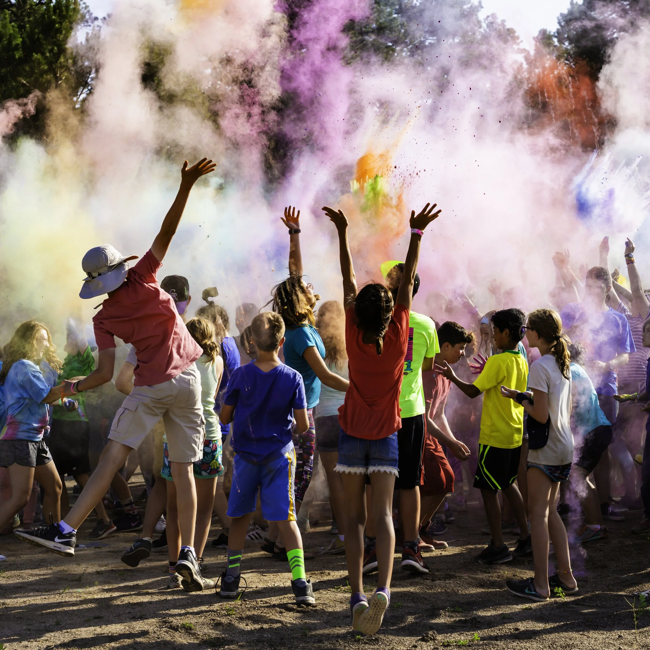 A large group of children outdoors celebrating the Holi festival with colorful powders in the air.
