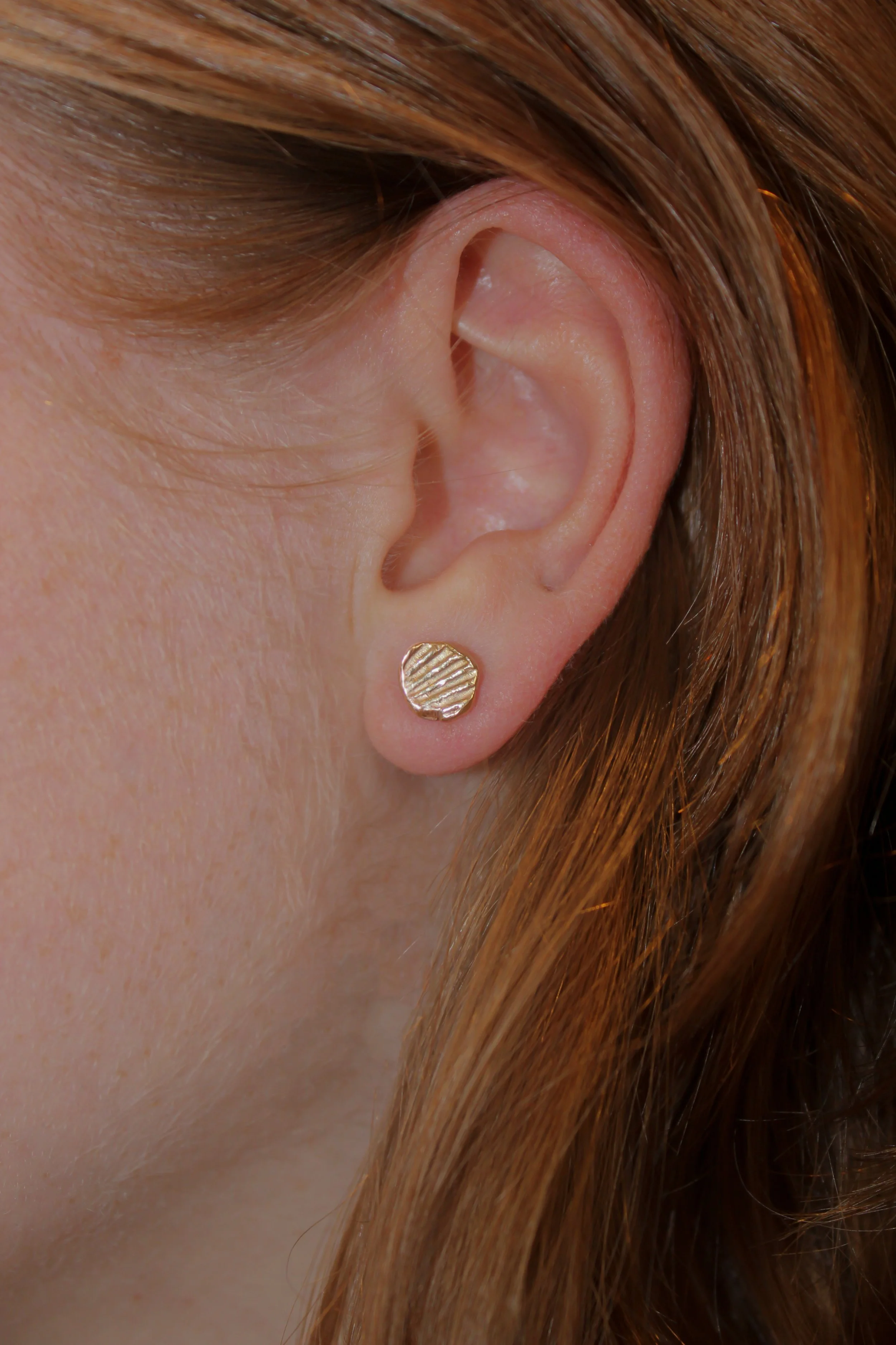 gold stud earring imprinted from seashells worn on a model's ear