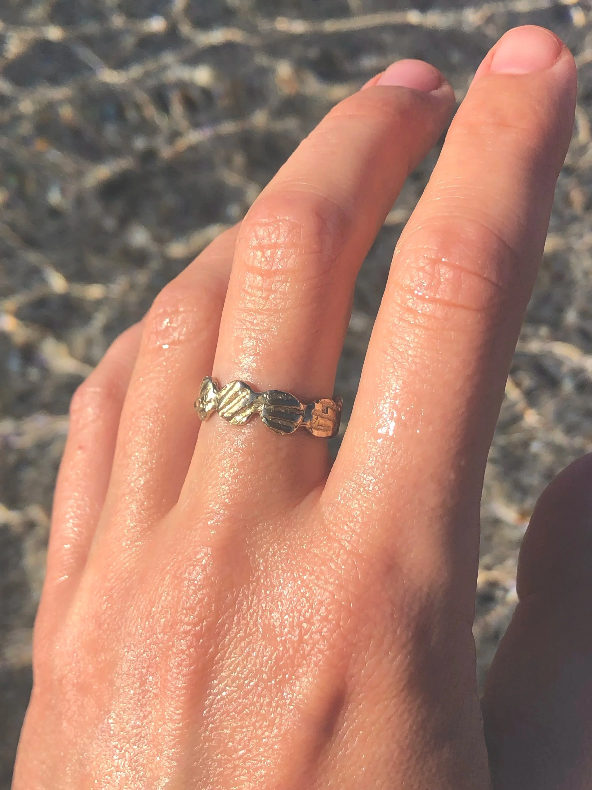 gold ring with design imprinted from seashells on model's hand at the ocean