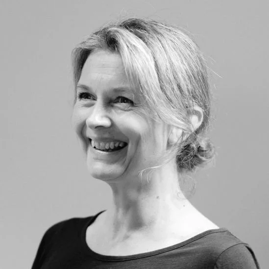 Black-and-white photo of a smiling woman with her hair in a loose bun, wearing a dark top.