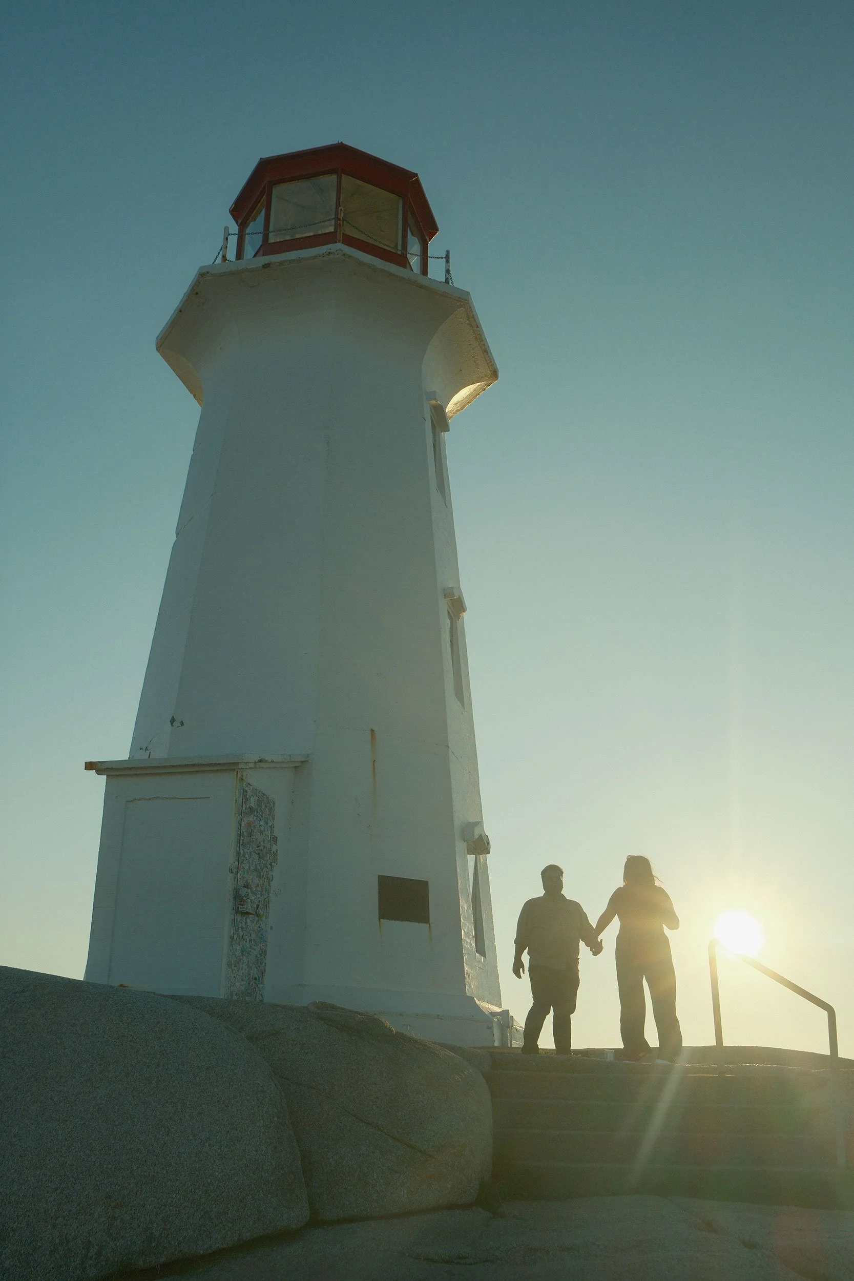 Peggy's Point lighthouse. Two people holding hands walking during sunset.