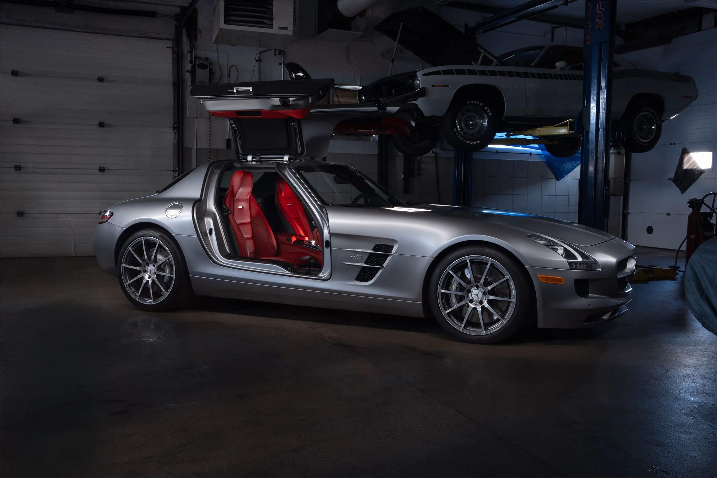 A matte silver 2011 Mercedes-Benz SLS AMG car with a red interior in a garage.