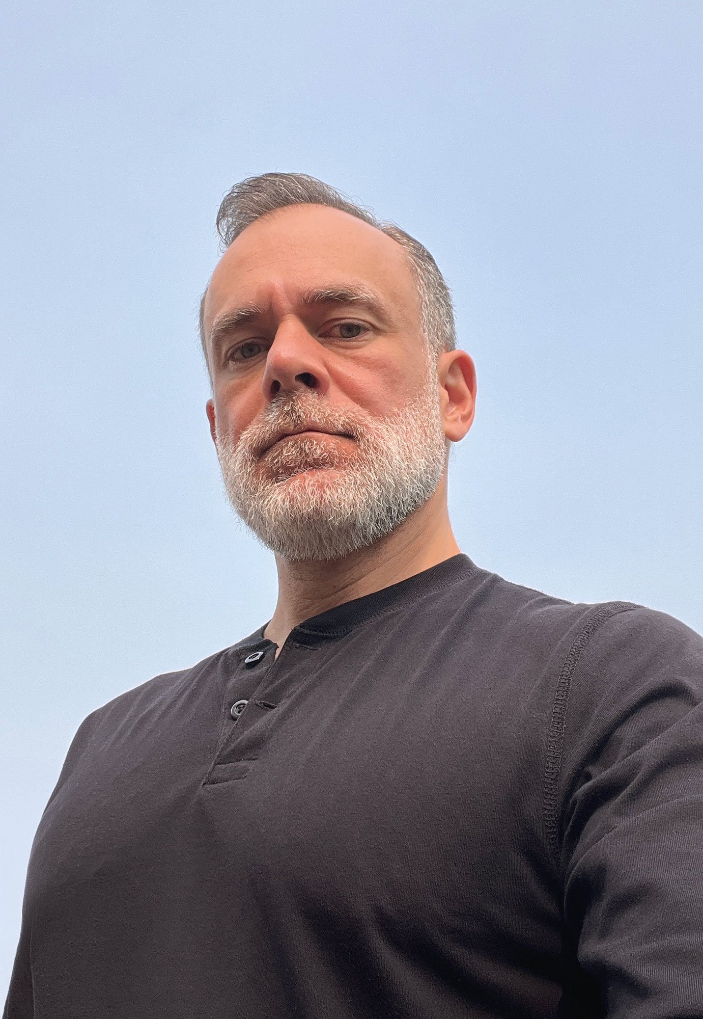 Tom England self-portrait. Dark button-up shirt, standing outdoors against a clear sky.
