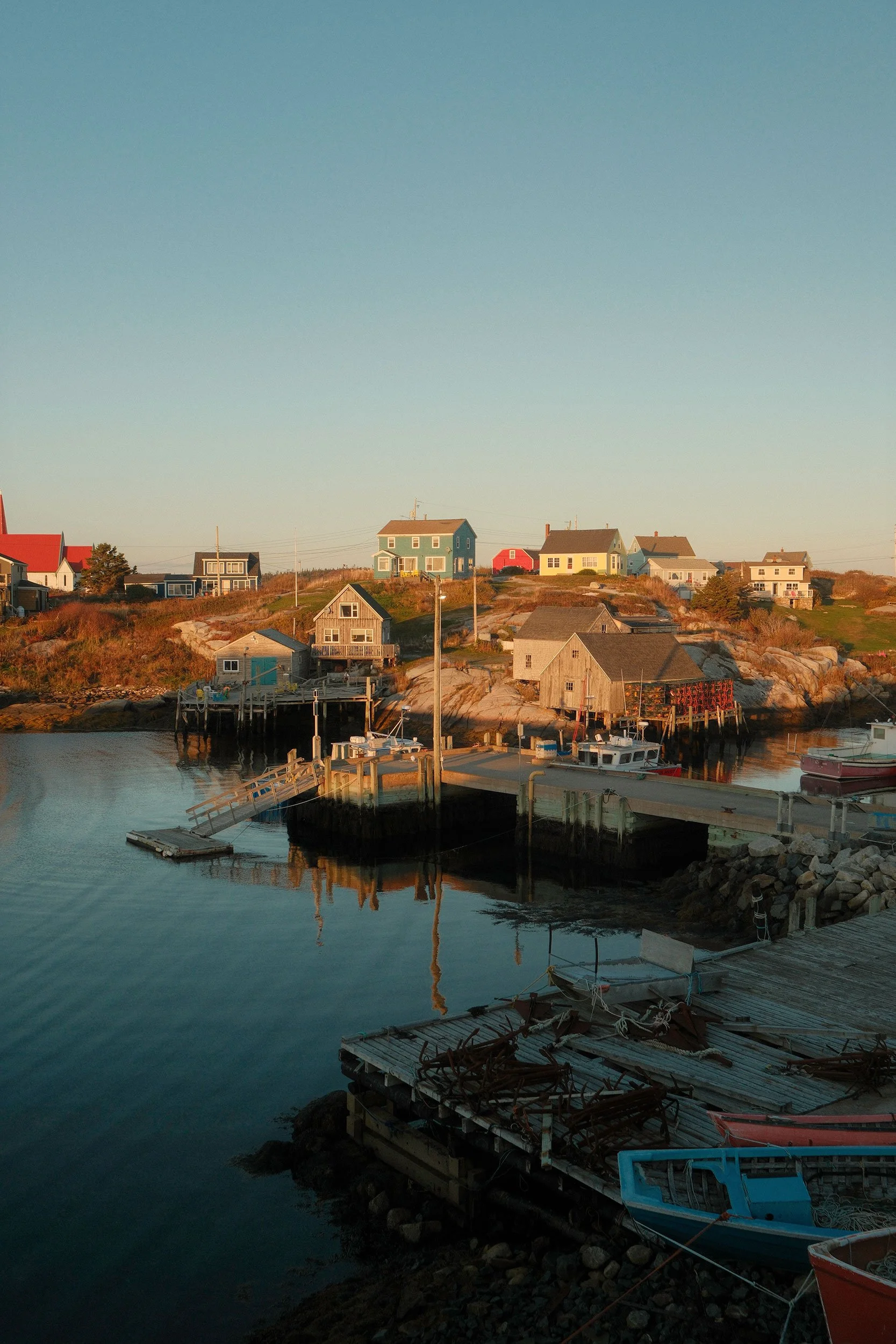 Colorful coastal fishing village with wooden homes, docks, fishing boats, and calm harbor water at sunset