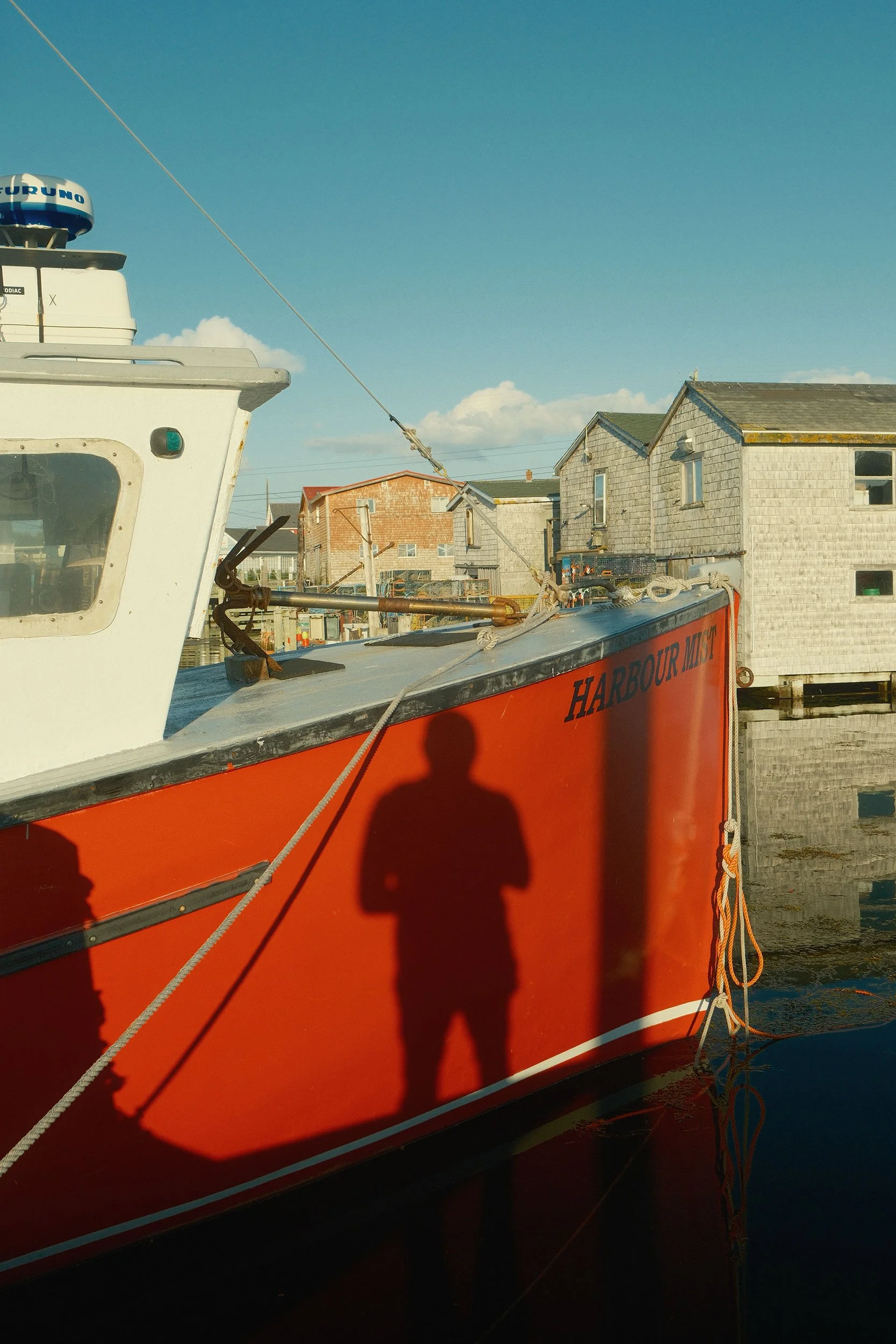 A bright orange boat docked in Peggy's Cove. Shadows of one person cast on its side.