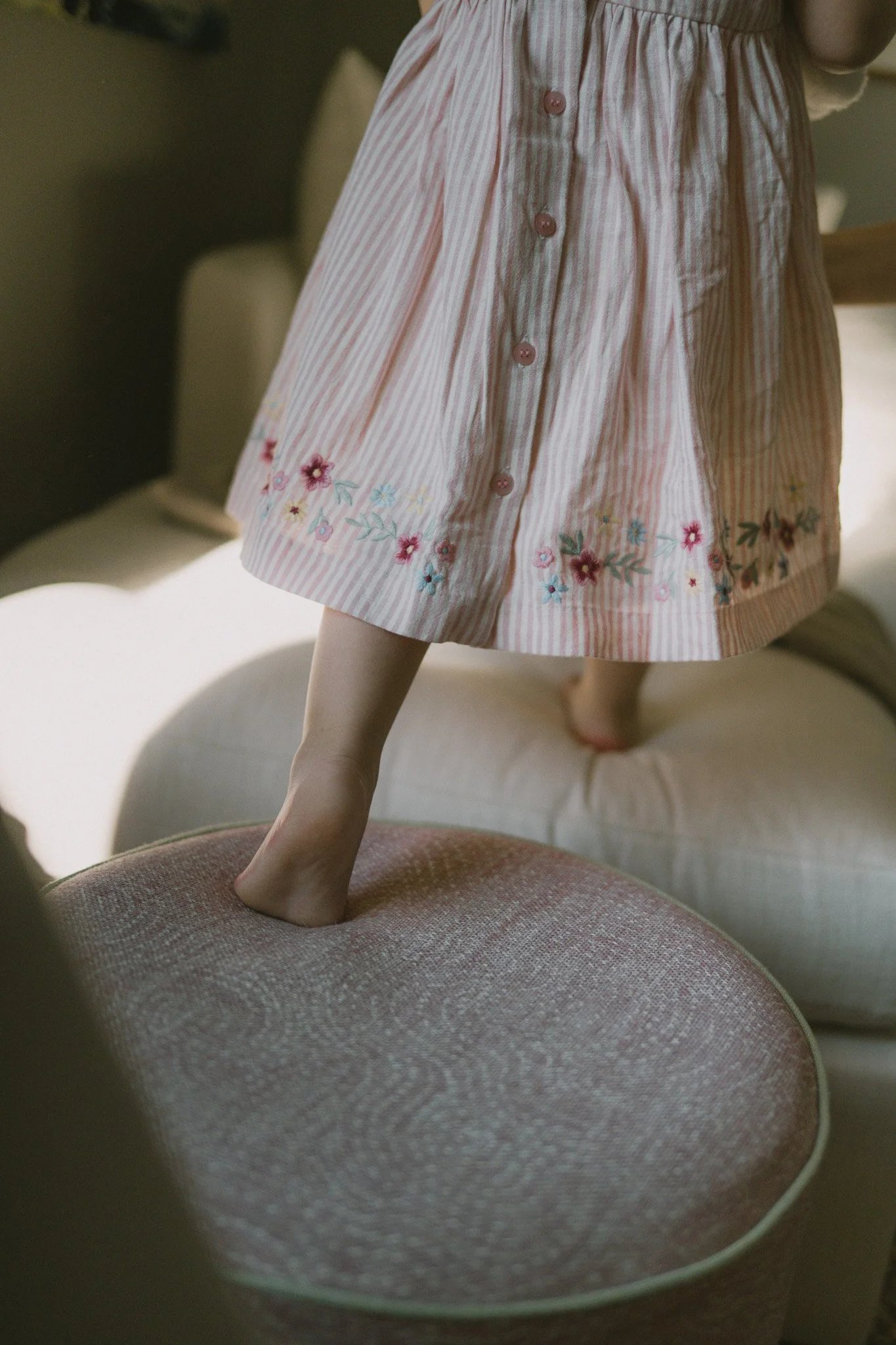 Barn på ett bord, klädd i ett rosa och vitt randigt klädesplagg med blommönster, som får ett ben att sticka ut.