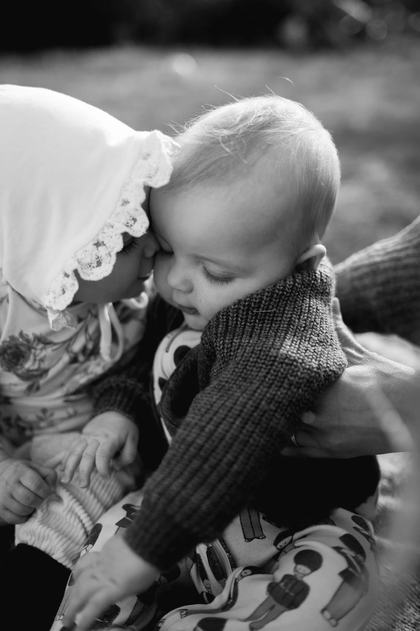 Två barn nära varandra, ett med huvudet täckt av en hoodie med spetsdetaljer, och ett med blont hår, som rör vid pannan och ögonen på varandra.