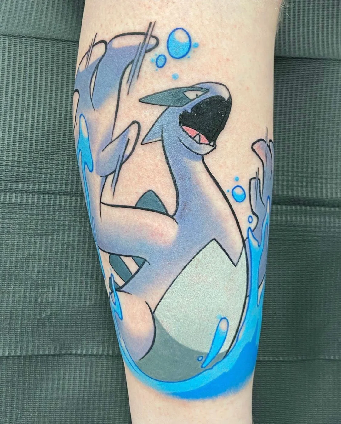 Tattoo of a stylized creature with blue and white colors, resembling a dragon, surrounded by splash effects and bubbles.