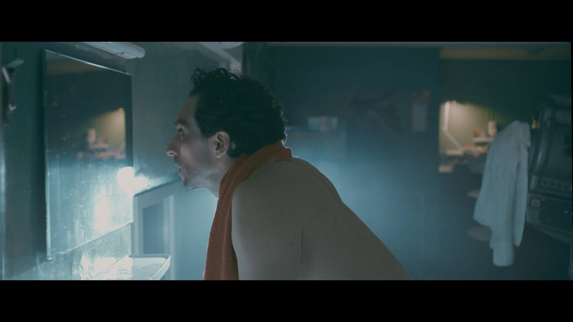 Ein Mann schaut in einen Wasserhahn in einer Küche, während Wasser spritzt, mit dunklem Hintergrund und Küchenutensilien.