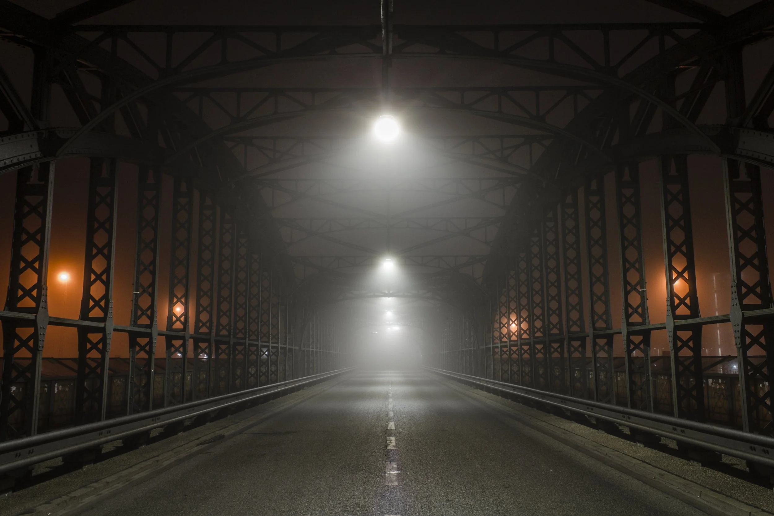 Nachtaufnahme einer leeren Brücke mit Lichtern und nebliger Atmosphäre.