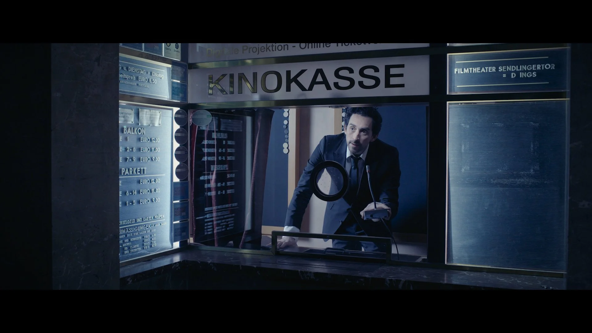 Ein Mann in formeller Kleidung, der an einem Kinokassenschalter steht, während er mit einem Kartenlesegerät arbeitet.