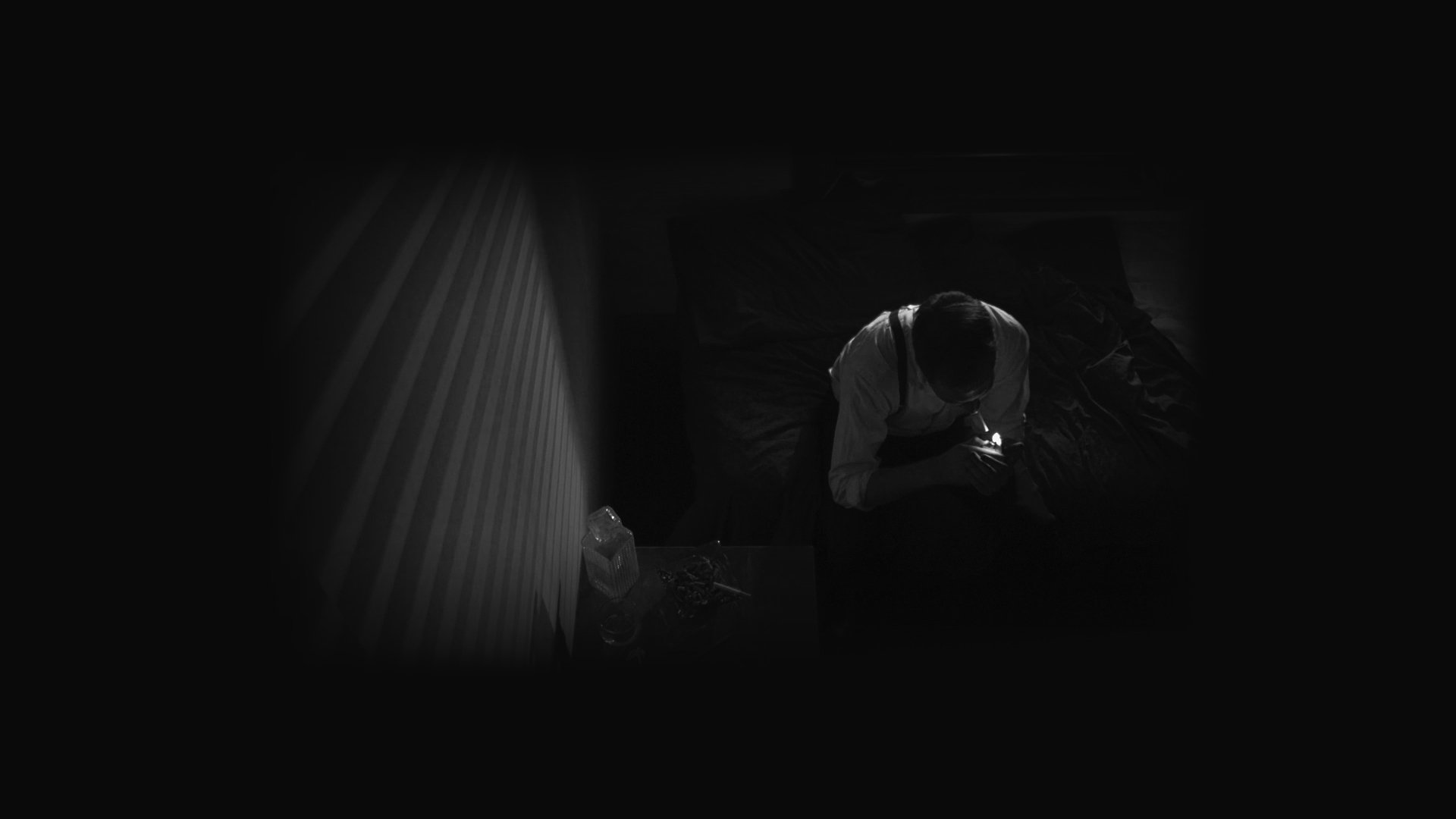 Ein Mann sitzt im dunklen Zimmer bei schwachem Licht, das von einem mobilen Gerät ausgeht.