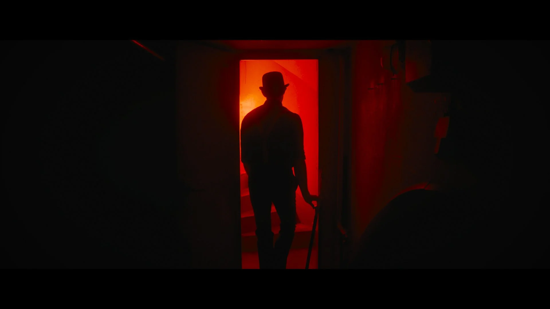 Eine Silhouette eines Mannes mit Hut, der in einen Raum mit rotem Licht geht.