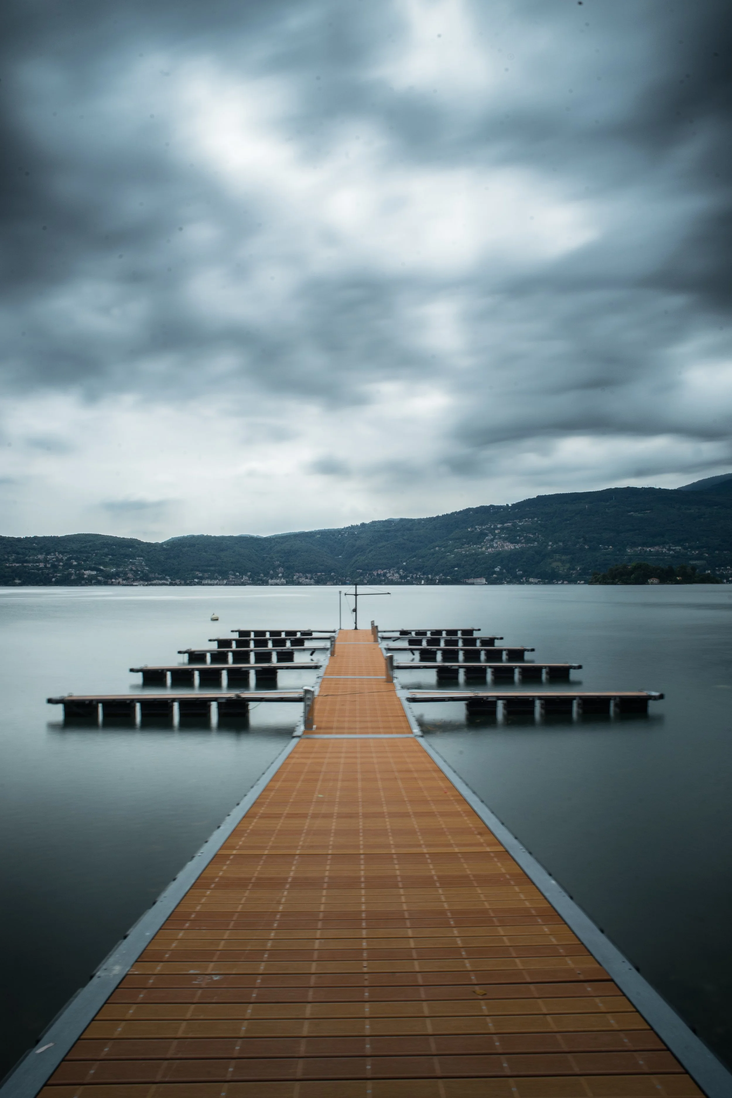 Ein Steg auf einem ruhigen See unter einem bewölkten Himmel, mit Bergen im Hintergrund.