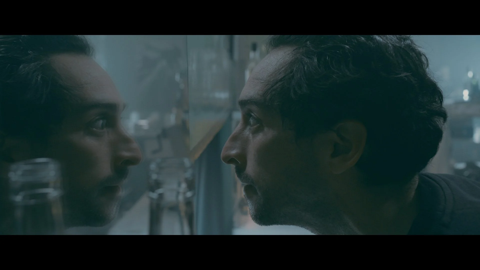 Nahaufnahme eines Mannes und einer Frau, die sich auf der anderen Seite einer Glasscheibe gegenüberstehen, beide schauen sich intensiv an.