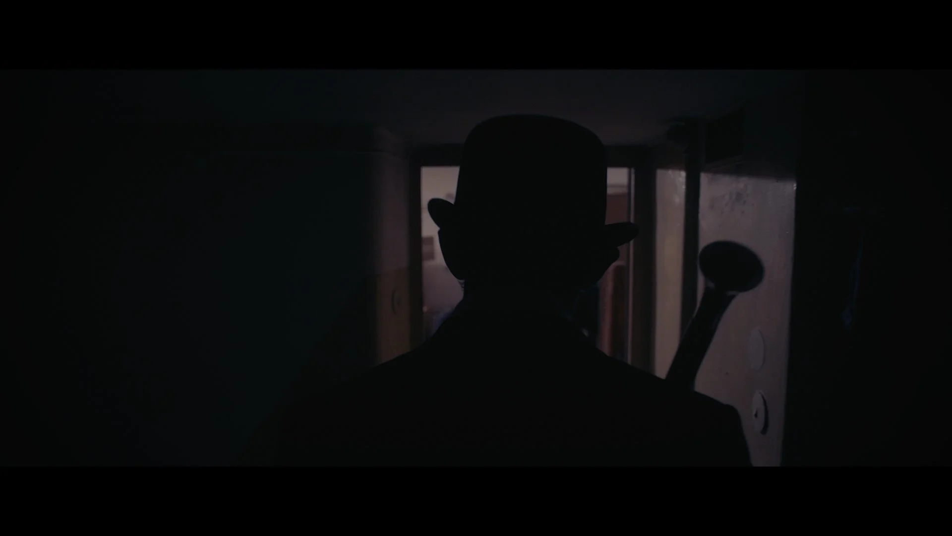 Schattenspiel einer Figur mit Zylinder und Stab vor einem dunklen Hintergrund, am Eingang eines Raumes