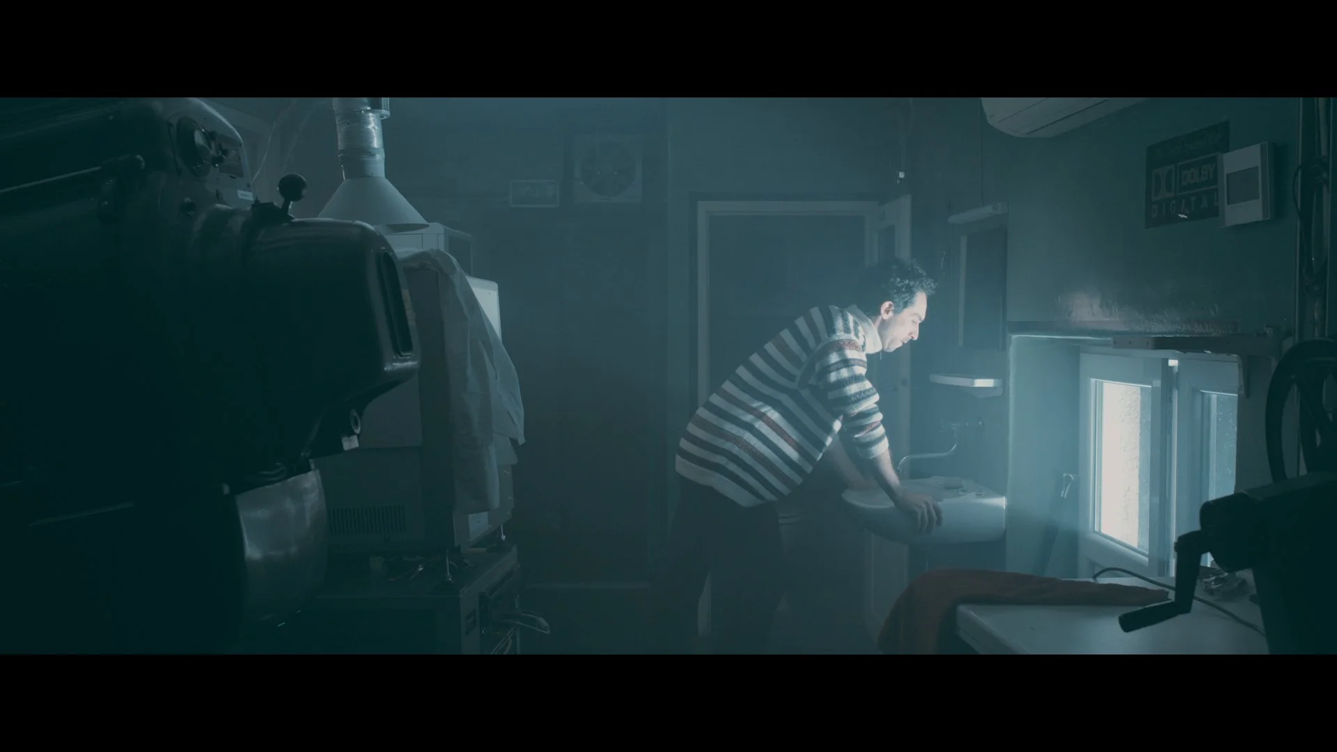 Ein Mann in gestreiftem Pullover wäscht sich die Hände an einem Waschbecken im Küchenraum, während Sonnenlicht durch das Fenster fällt.