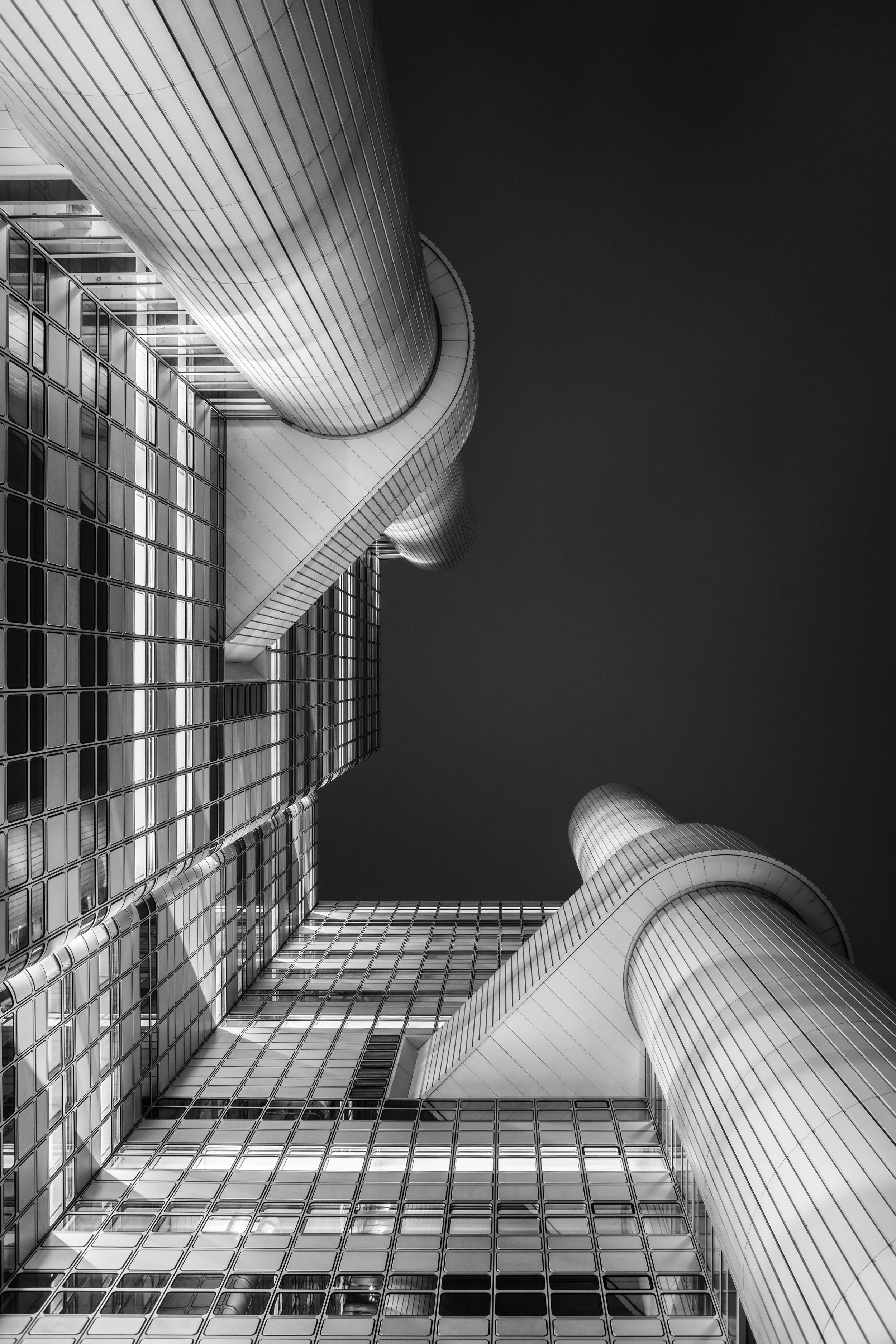 Abstrakte schwarze und weiße Aufnahme eines modernen Hochhauses mit zylindrischen und rechteckigen Elementen, aufgenommen von unten nach oben.