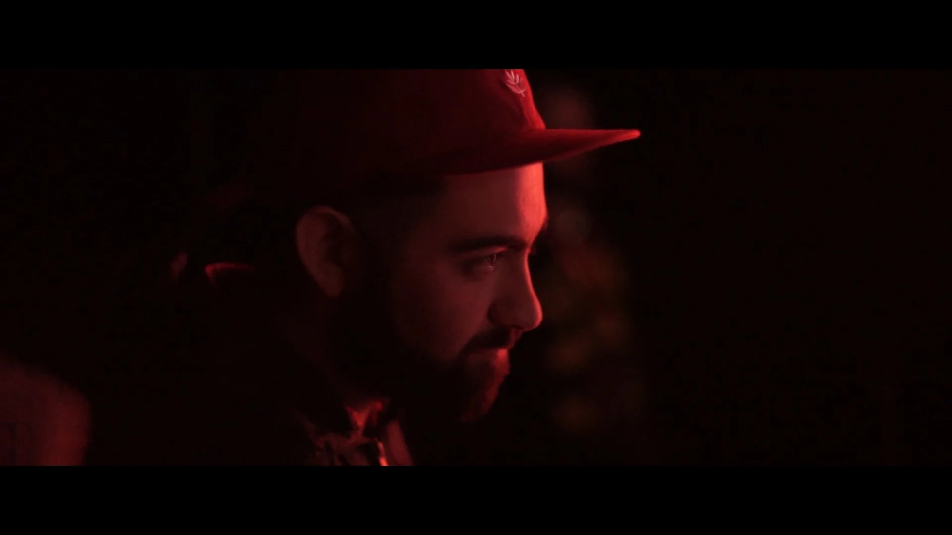 Nahaufnahme eines Mannes in einem dunklen Raum, der eine rote Mütze trägt, bei schwachem rotem Licht