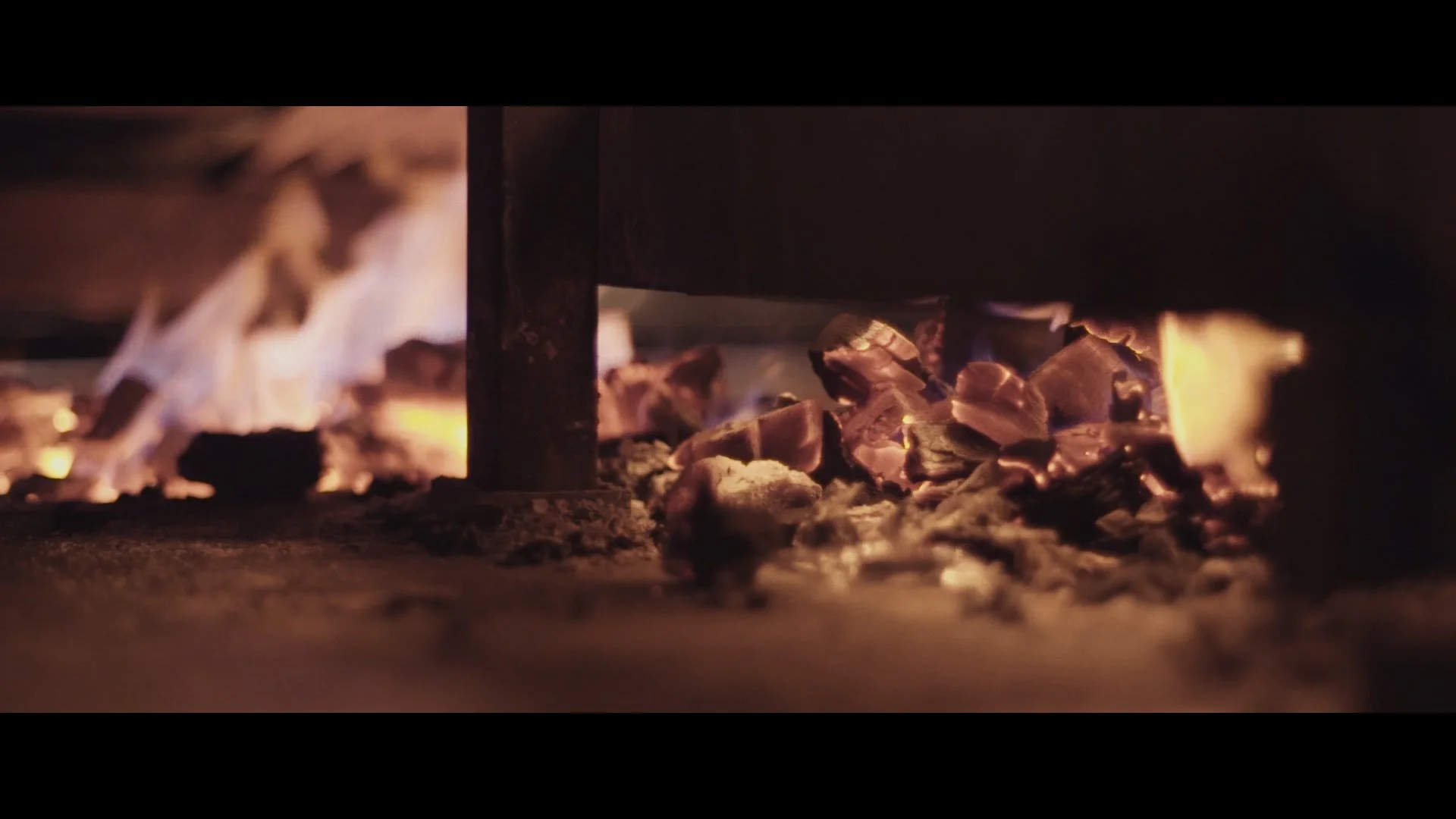 Brennende Kohle und Holzscheite unter einem Grillrost.