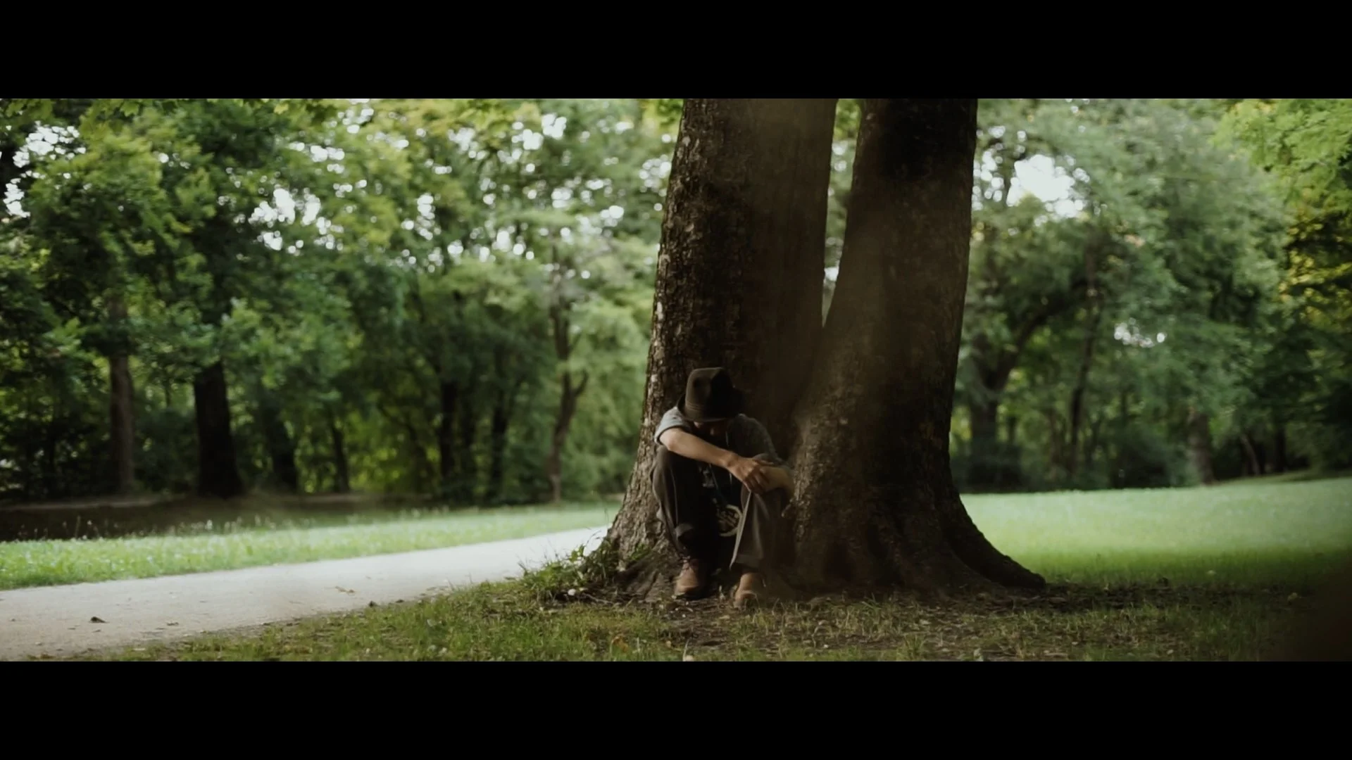 Person sitzt traurig am Baum im Park und trägt einen Hut.