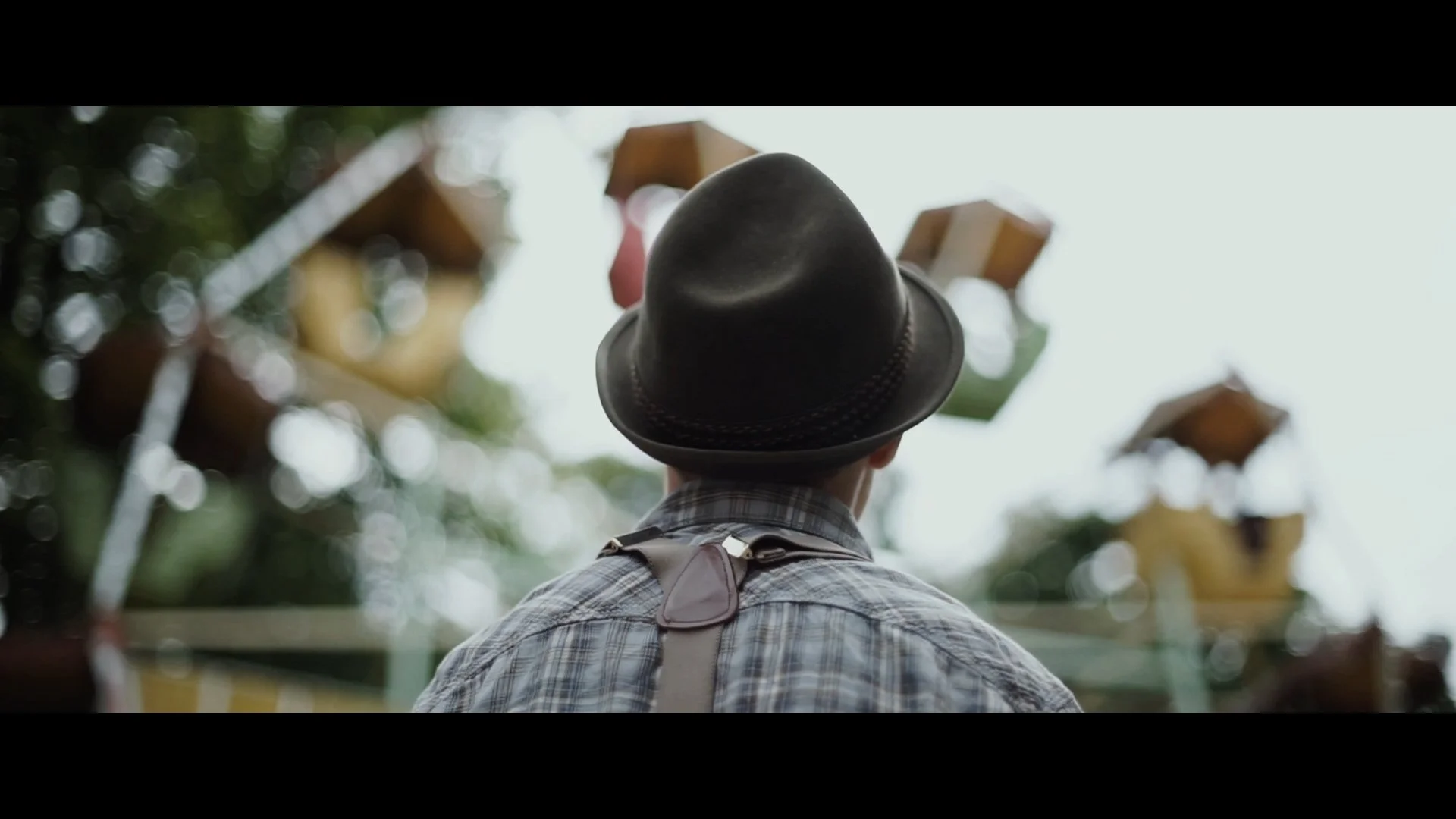 Ein Mann trägt einen schwarzen Hut und schaut sich die Achterbahn auf einem Jahrmarkt an.