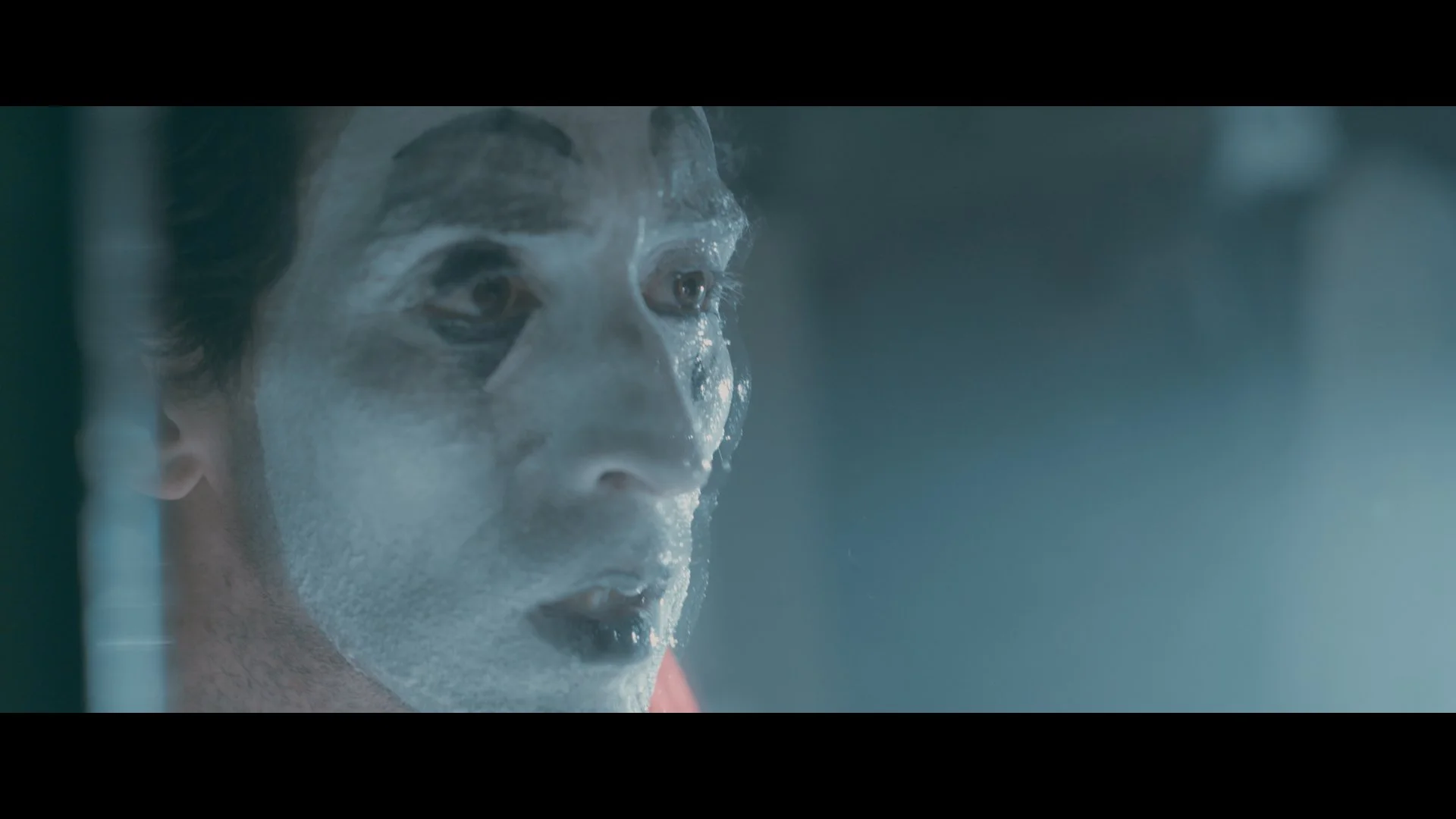 Nahaufnahme eines Mannes mit geschminktem Gesicht, das wie eine Eisschicht aussieht, in einem dunklen, unscharfen Hintergrund.