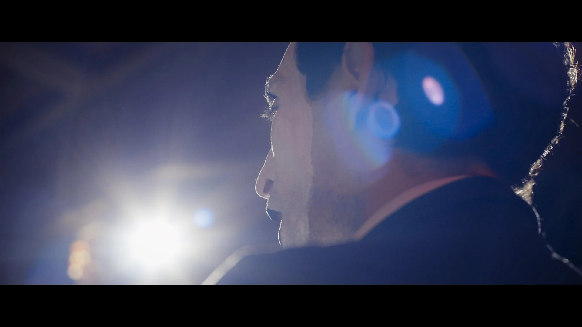 Nahaufnahme eines Mannes in einer dunklen Umgebung mit hellem Licht im Hintergrund, Blendung und Lichtreflexe auf dem Bild.