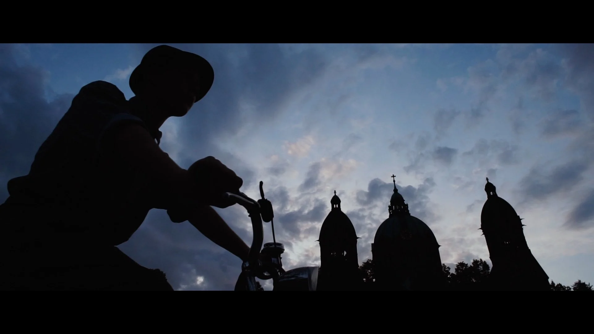 Schatten einer Person mit Fahrrad vor einer Skyline mit Kirchenkuppeln bei Sonnenuntergang