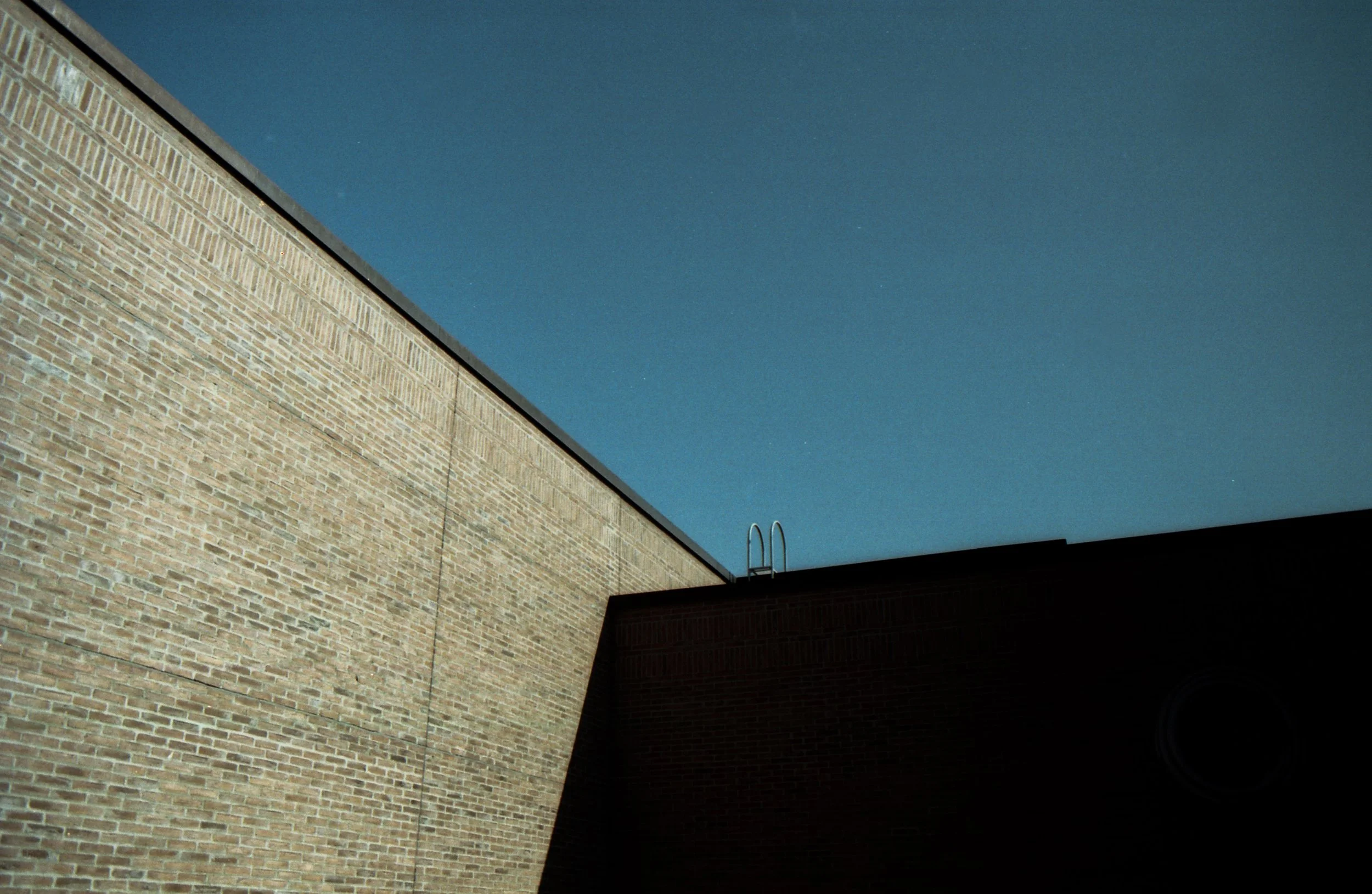 Blick auf die Ecken eines Gebäudes mit einer Leiter auf dem Dach, bei Tag mit klarem Himmel.